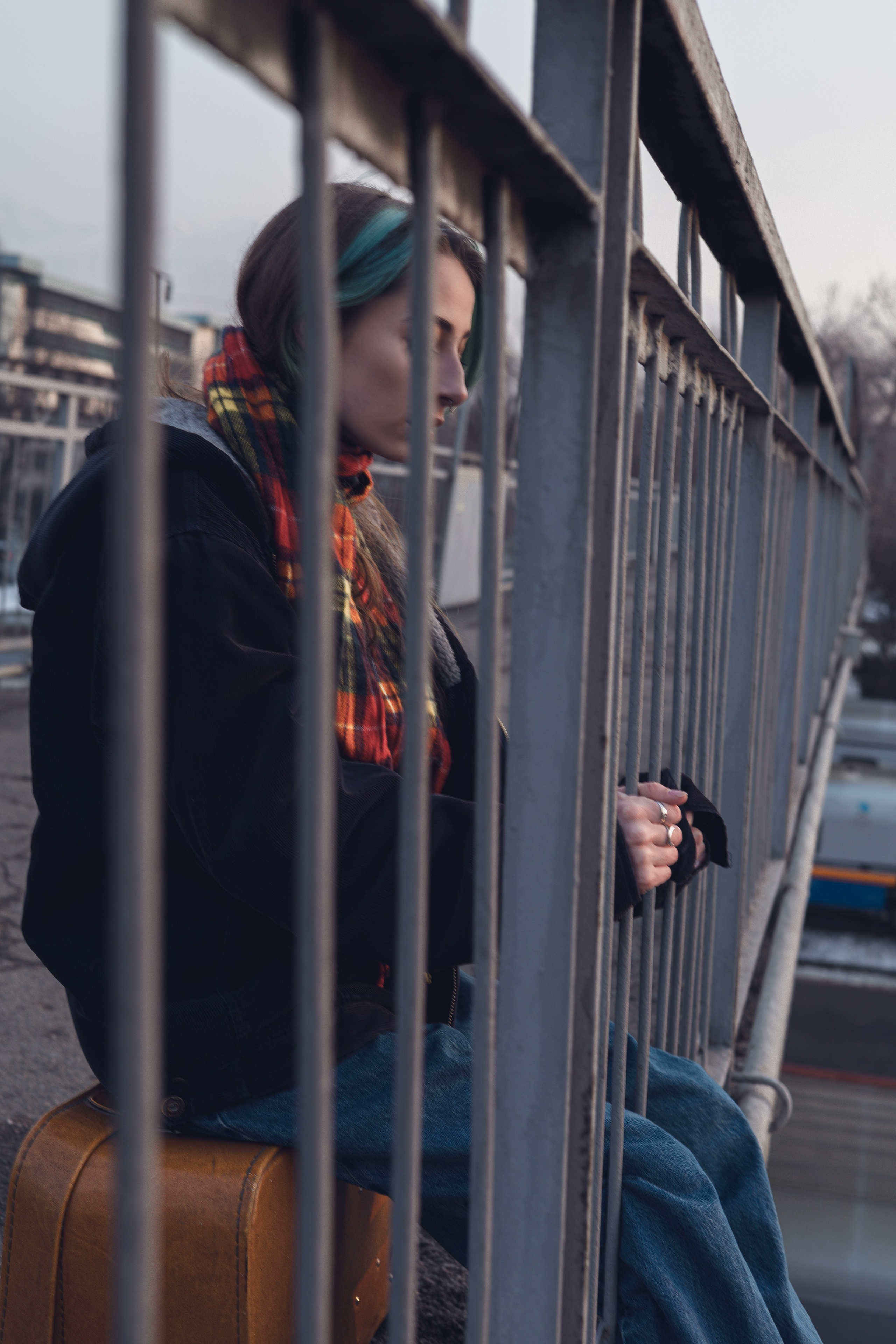 Фотосессия в городе: девушка в шарфе стоит у сетки забора