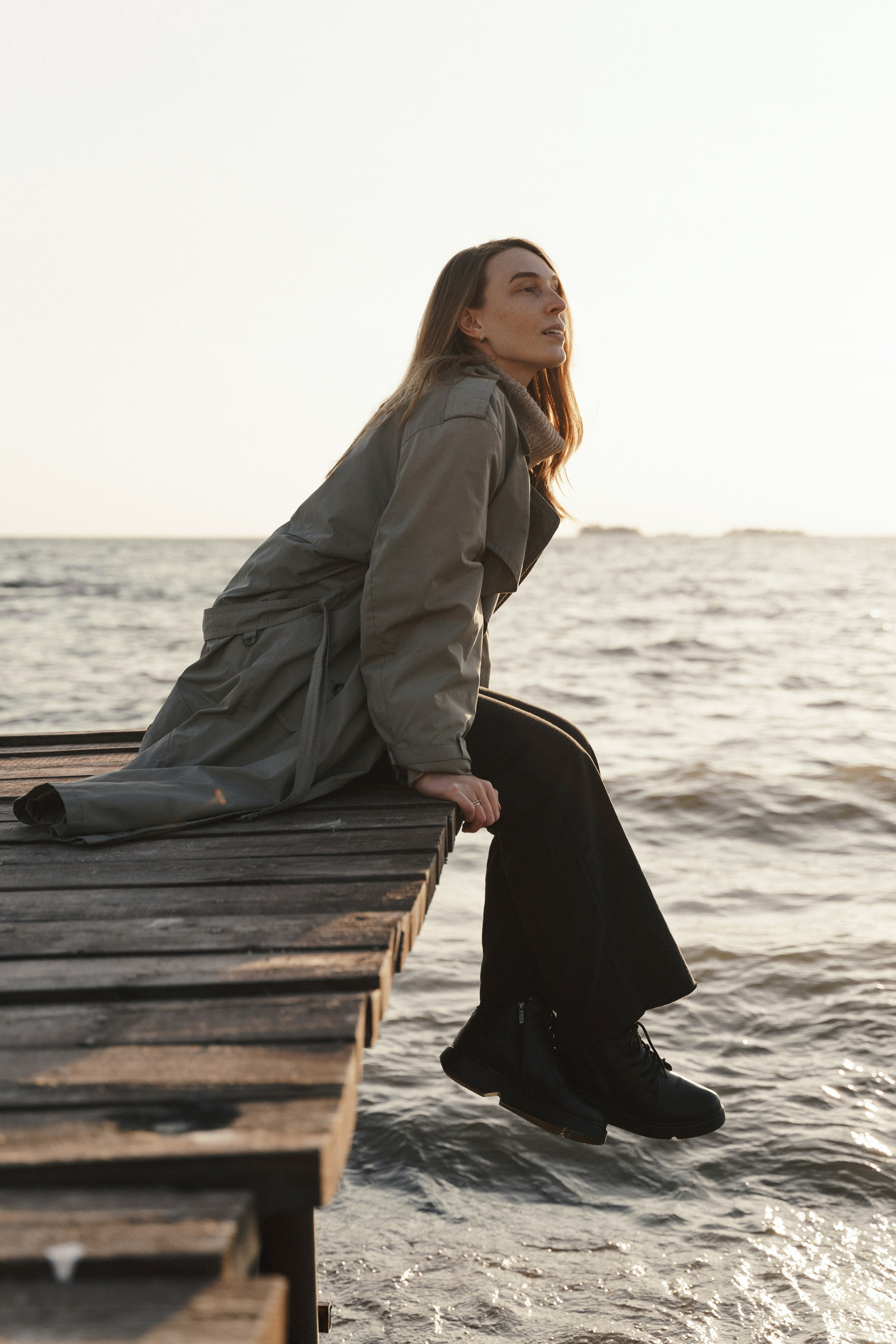 Девушка сидит на берегу реки летом на закате и смотрит вдаль