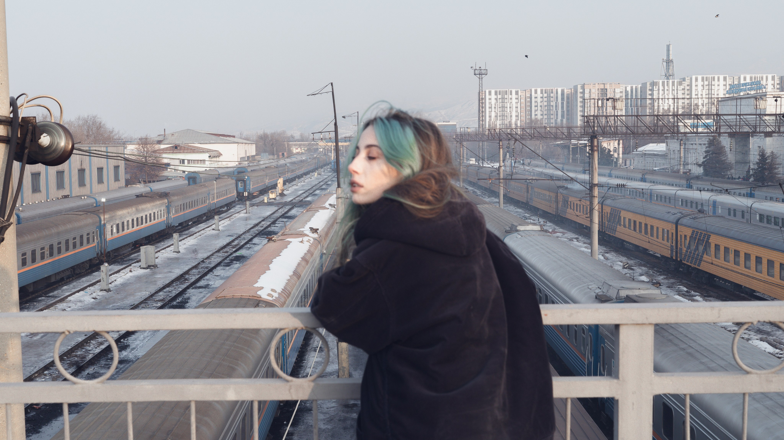 Девушка стоит у забора в лучах заката, взгляд в сторону