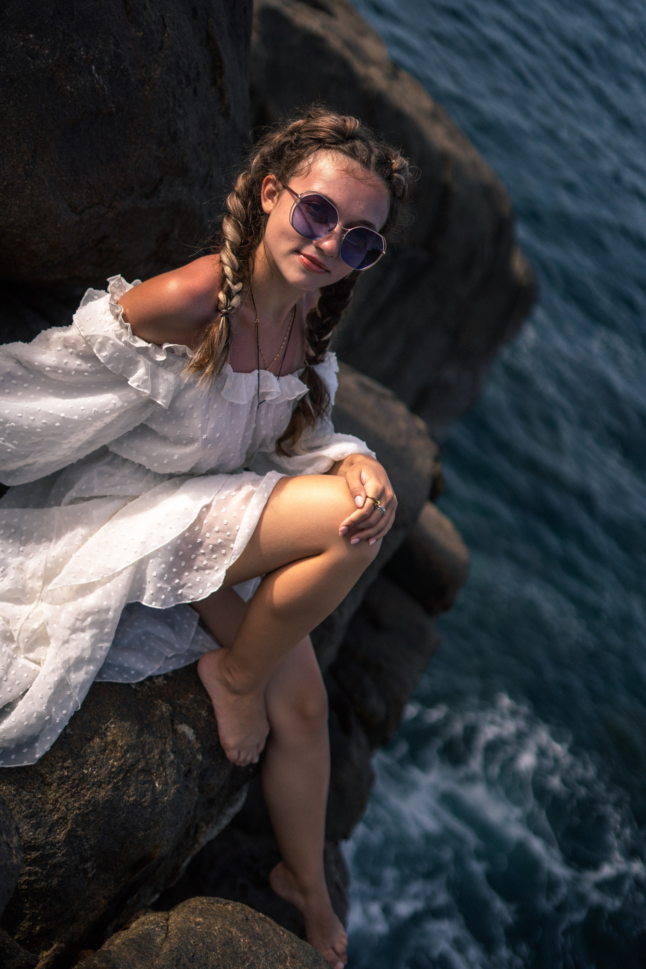 a girl in a white dress and glasses posing with seashells on the rocks