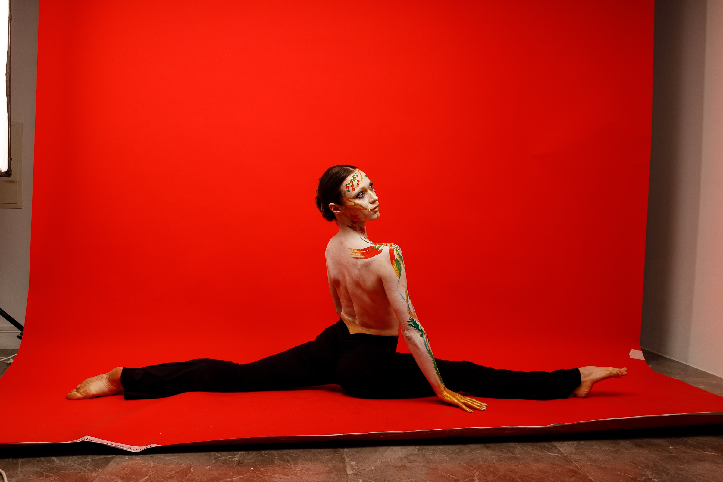 Обнаженная девушка села на шпагат на красном фоне