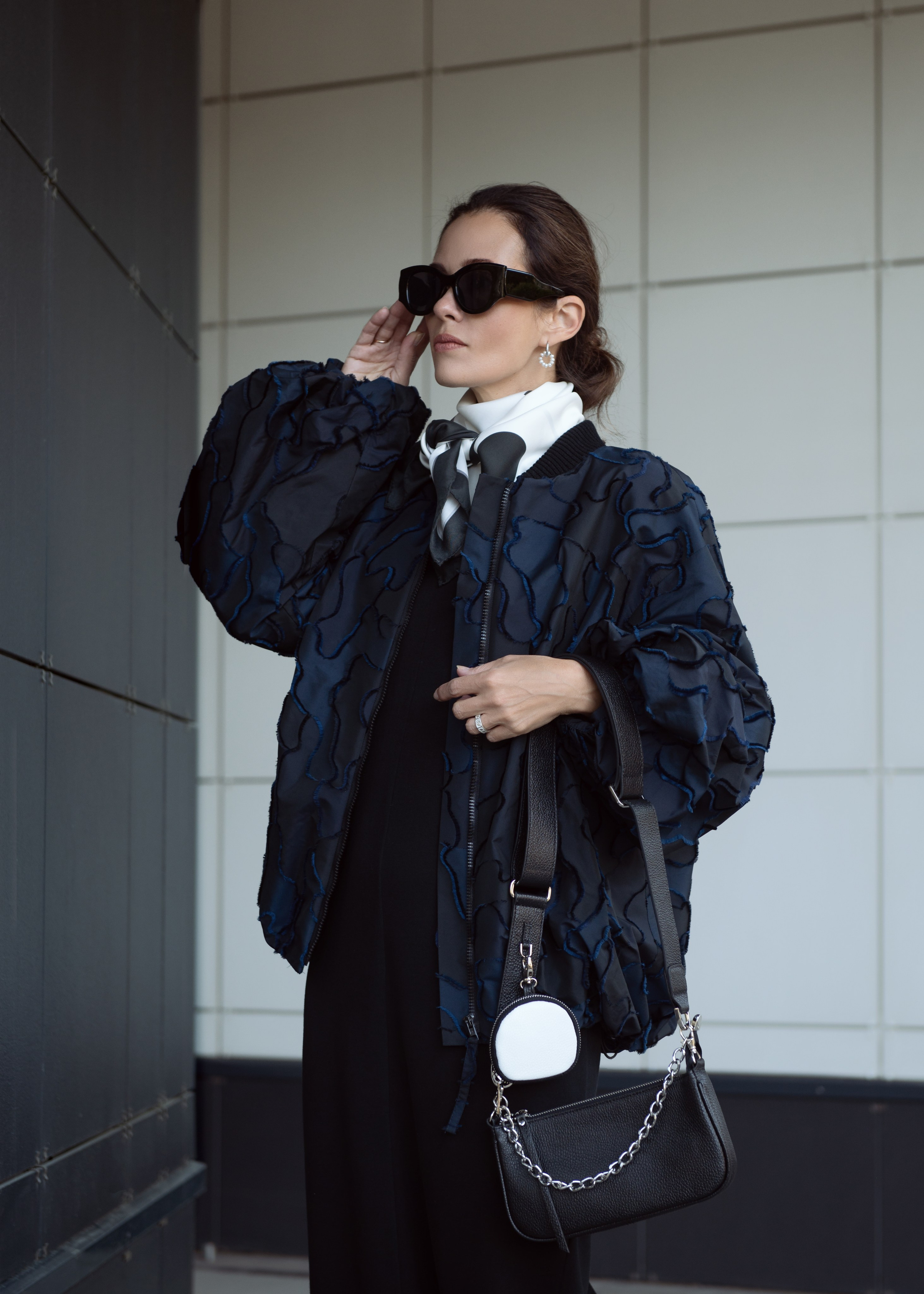 Темноволосая девушка поправляет очки. Съемка для магазина женской одежды и аксессуаров. Съемка на улице.