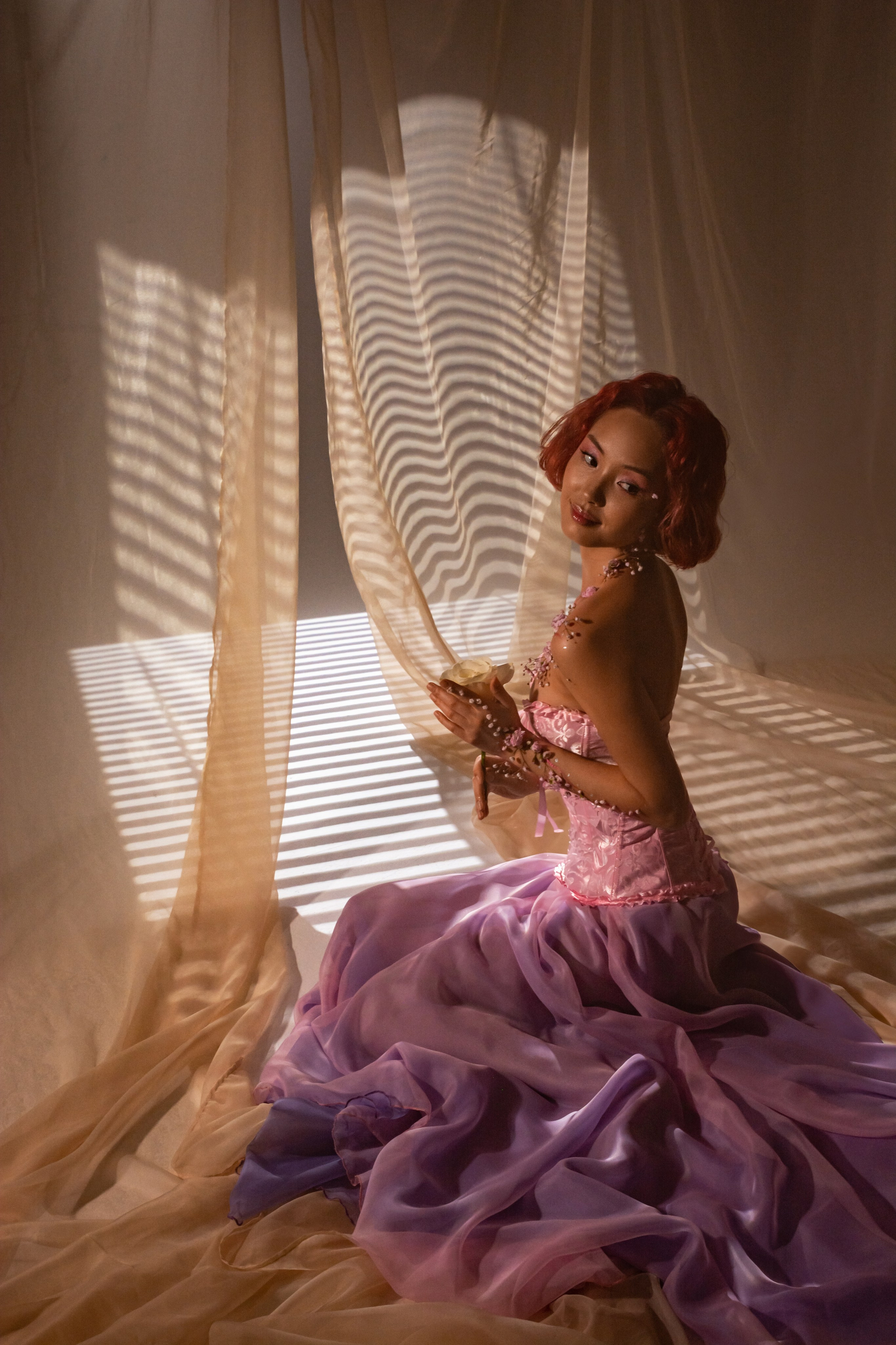 Купаясь в солнечном свете, льющемся из окна, хрупкая фигура девушки в цветочном розовом наряде олицетворяет приход долгожданной весны и пробуждение природы после зимних холодов.