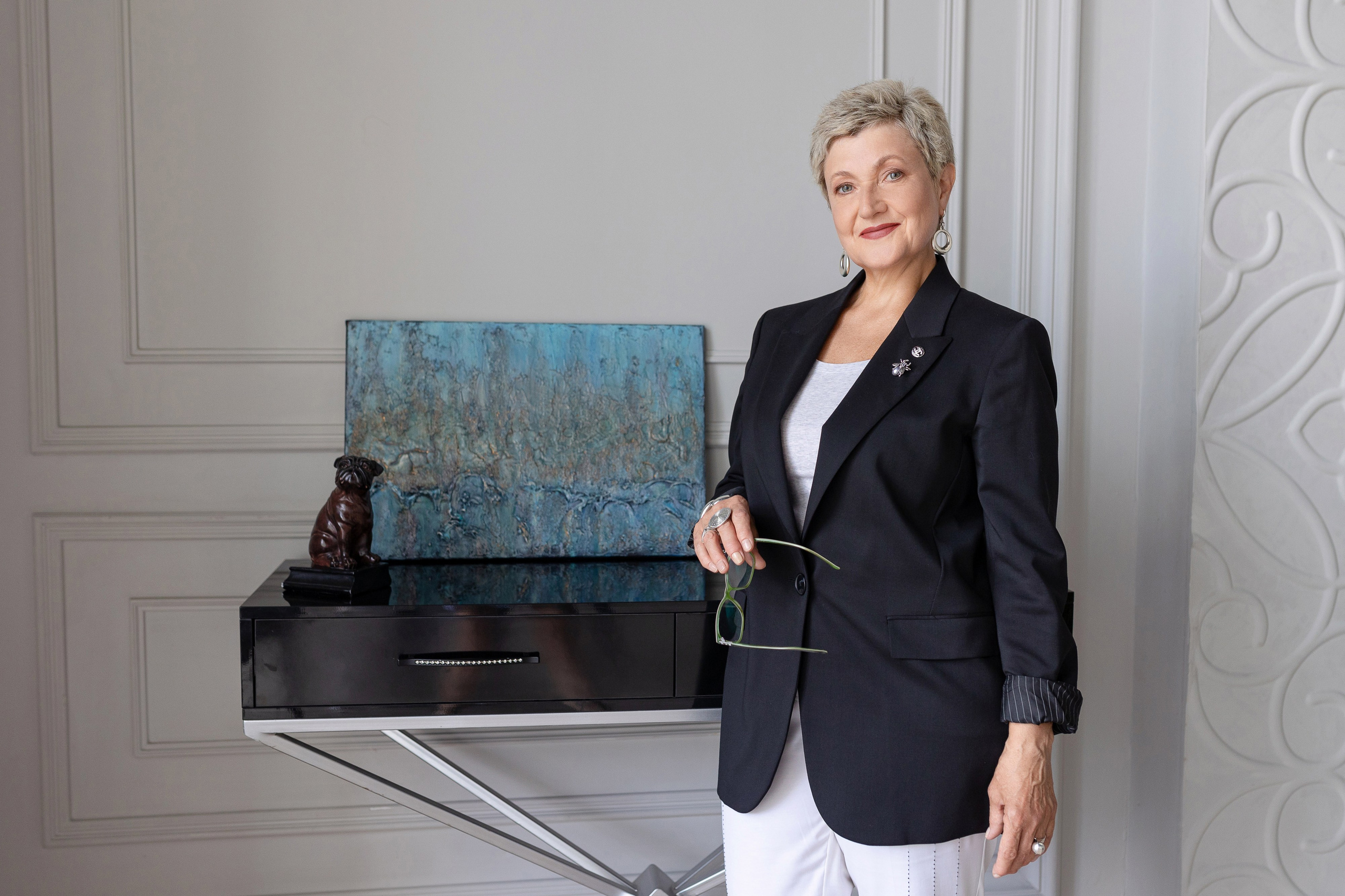 Художница стоит у стола, на котором находится картина в голубых тонах.