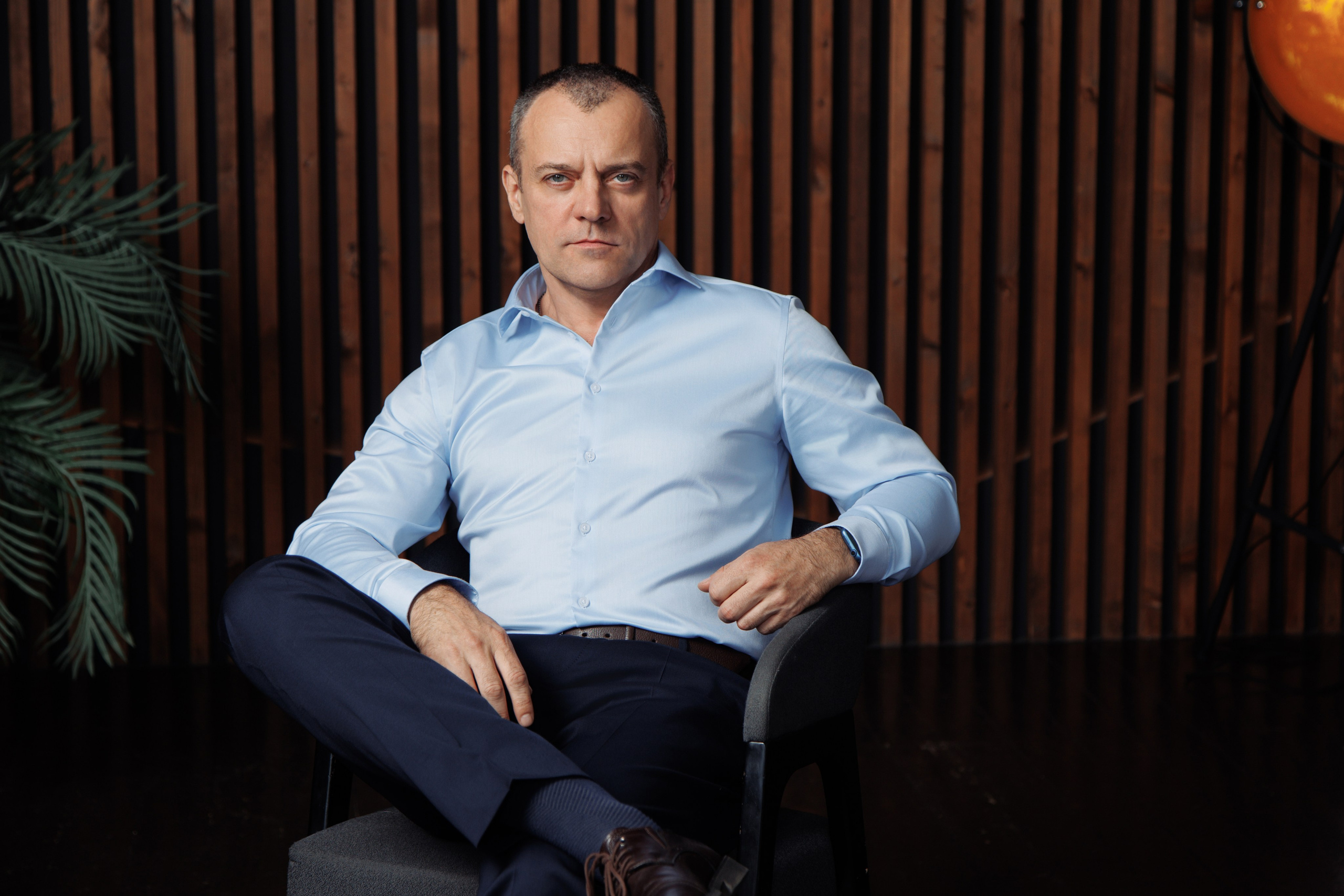 Мужчина в синей рубашке сидит на фоне современного светлого офиса.