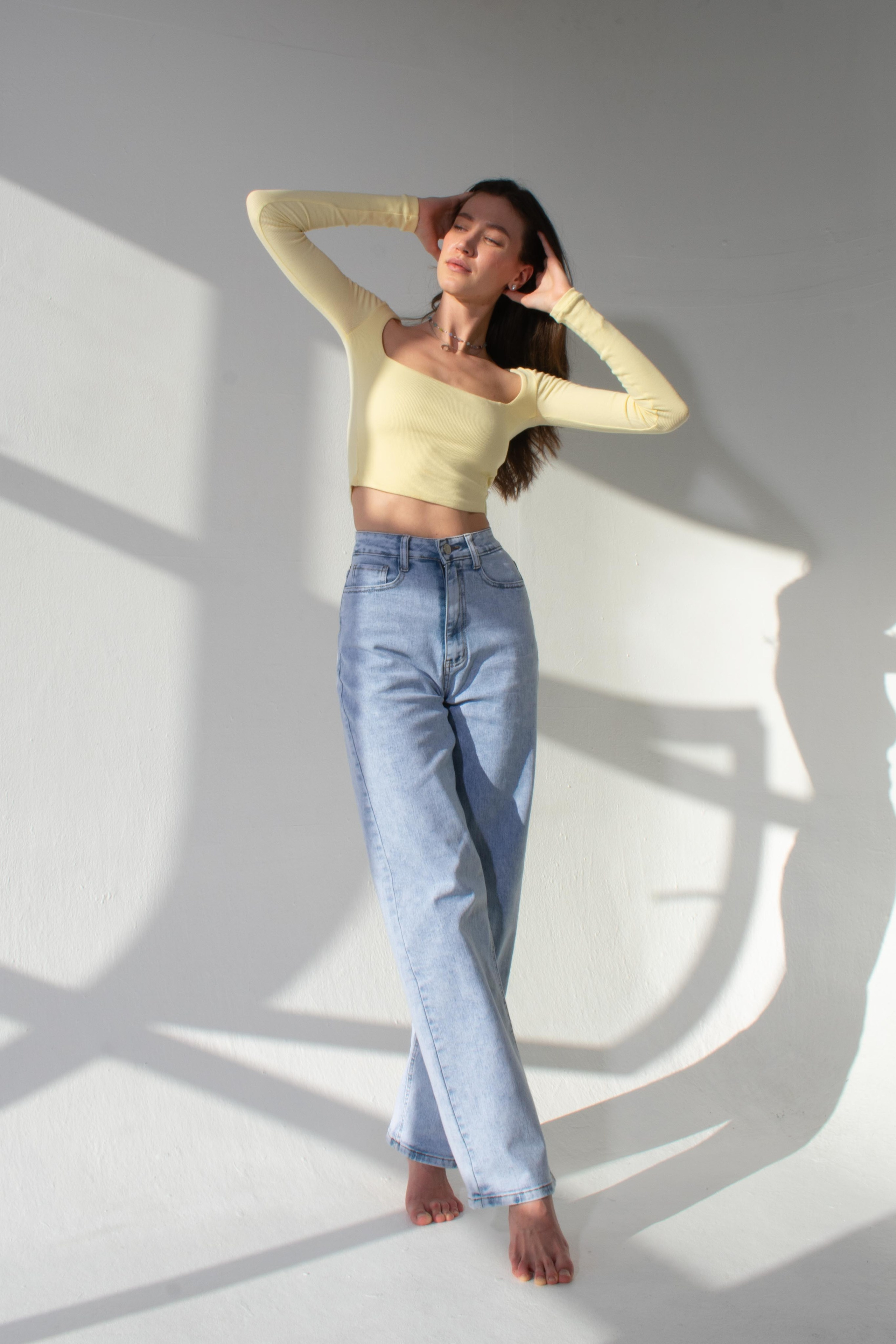 Модель позирует в солнечный день в студии в желтой футболке и джинсах