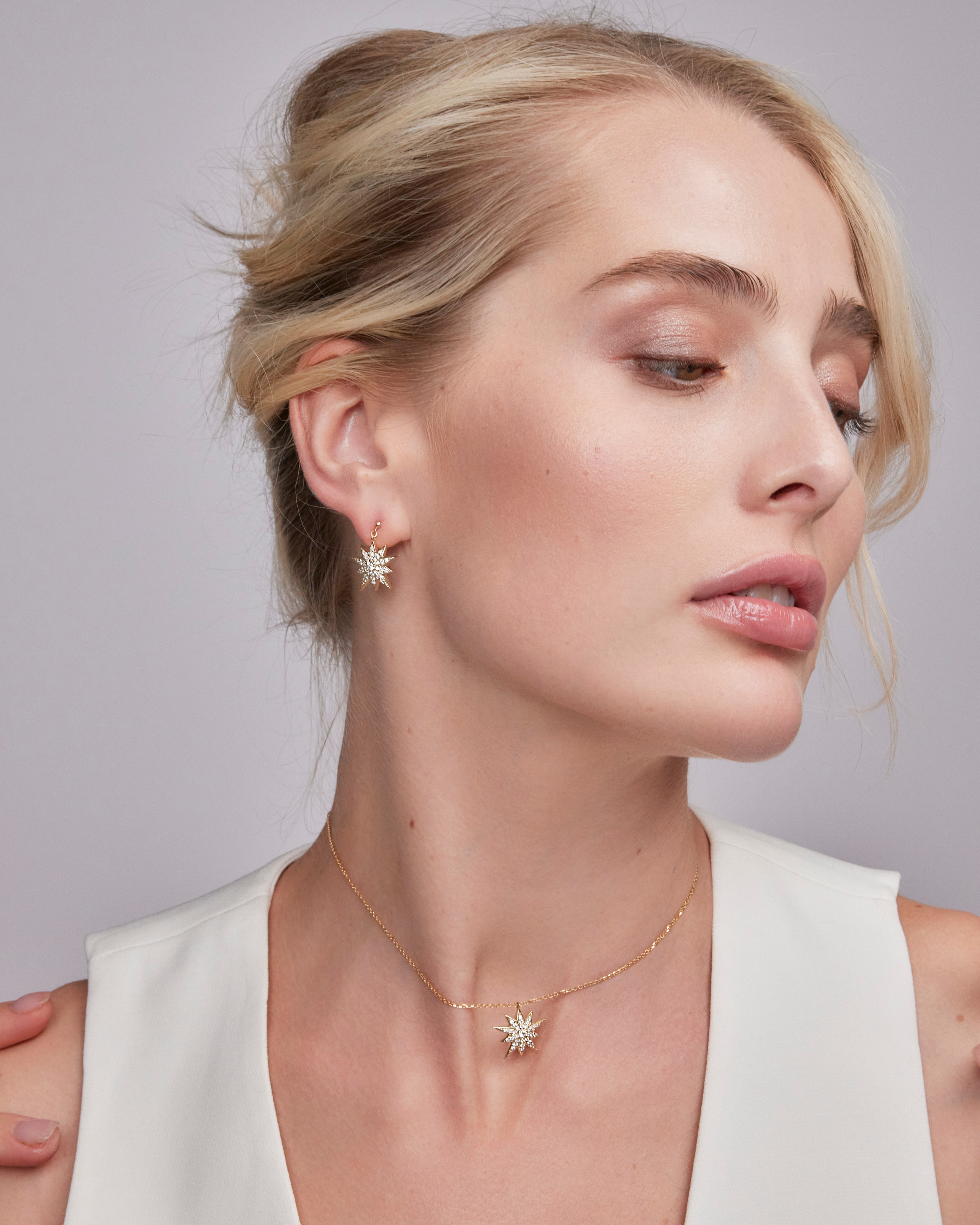 Blonde model wearing gold earrings and a necklace, paired with a white dress, emphasizing sophisticated jewelry styling.
