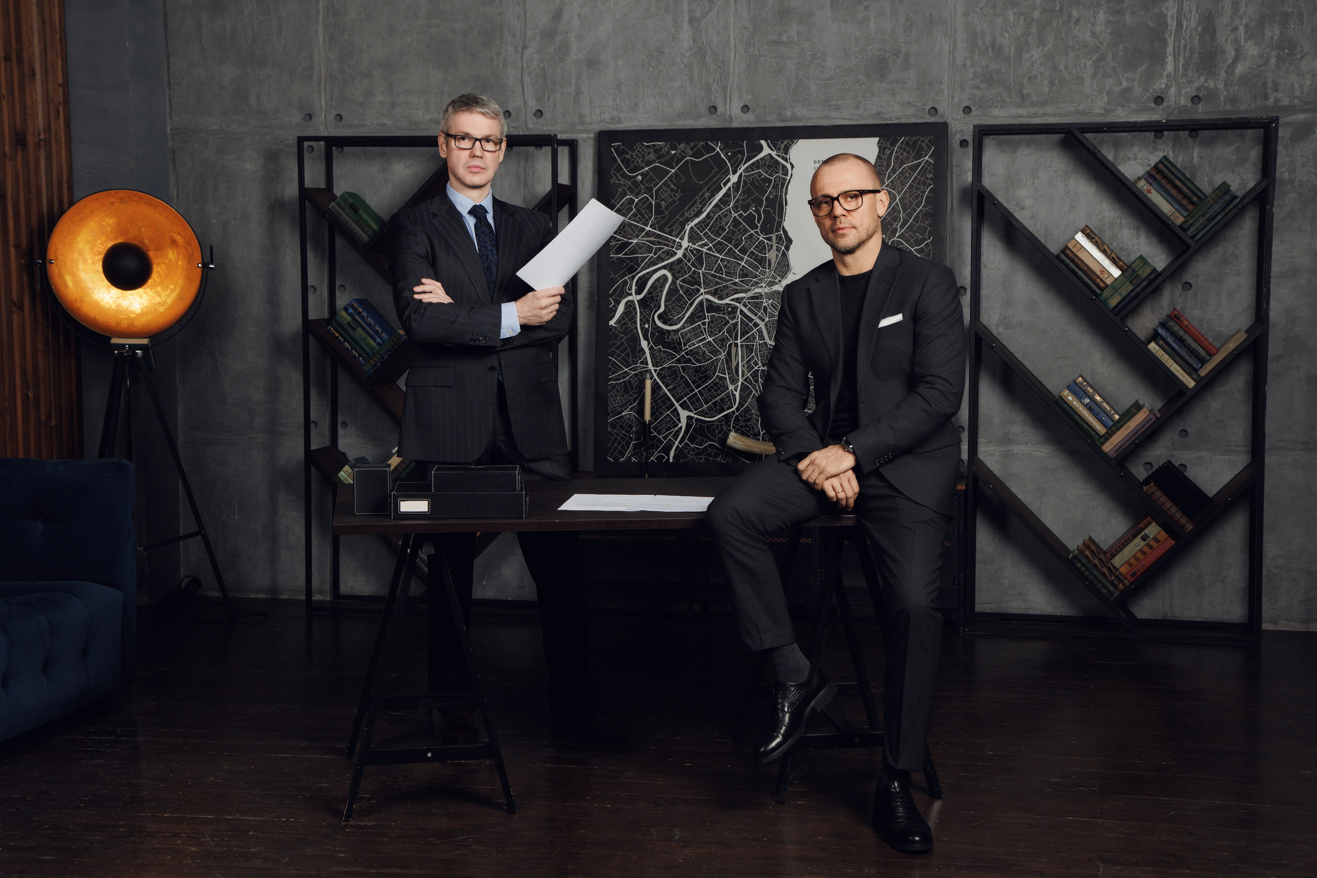 Двое коллег в деловой одежде стоят за рабочим столом во время обсуждения.