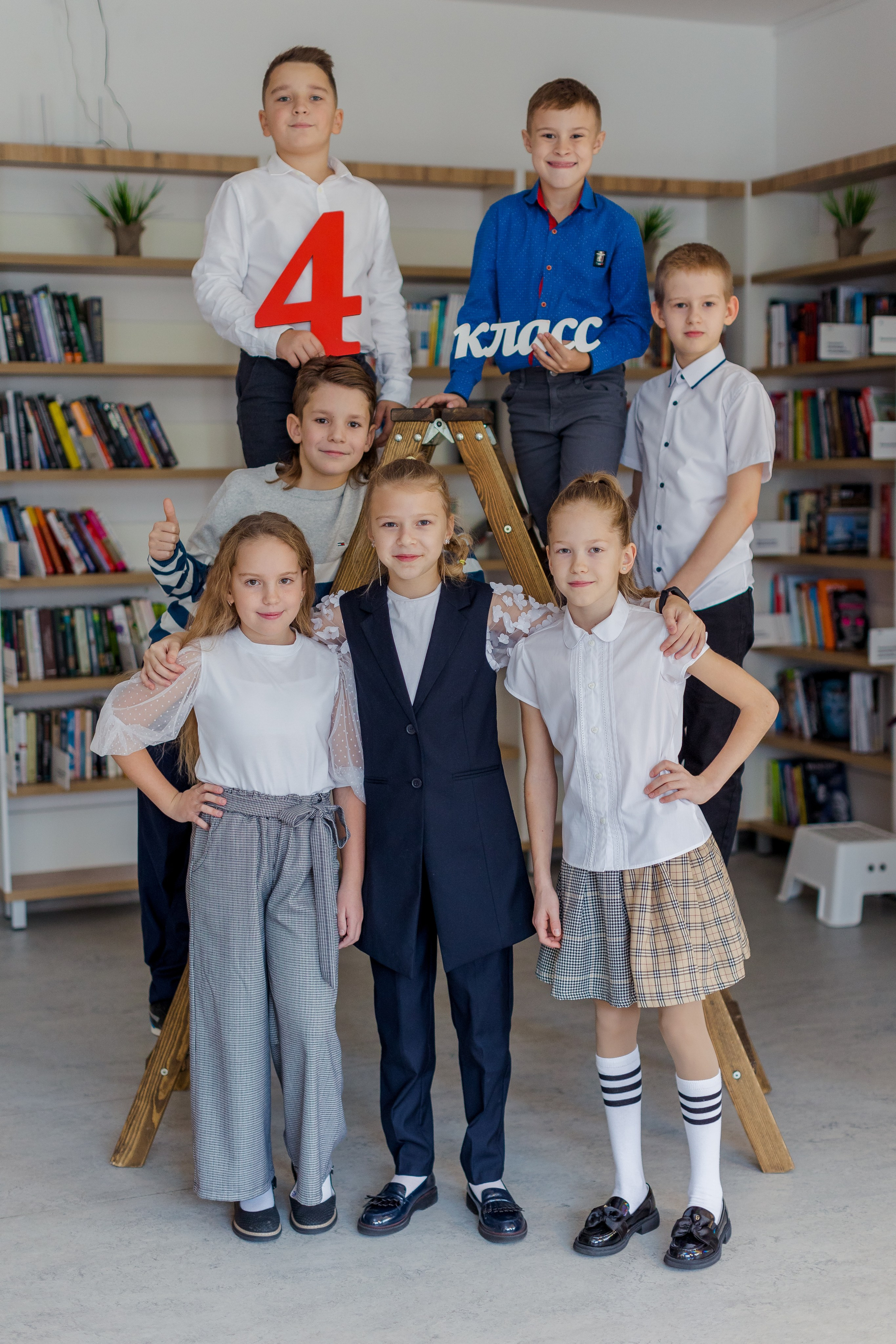 Девочки и мальчики стоят на лестнице в библиотеке с надписью 4 класс