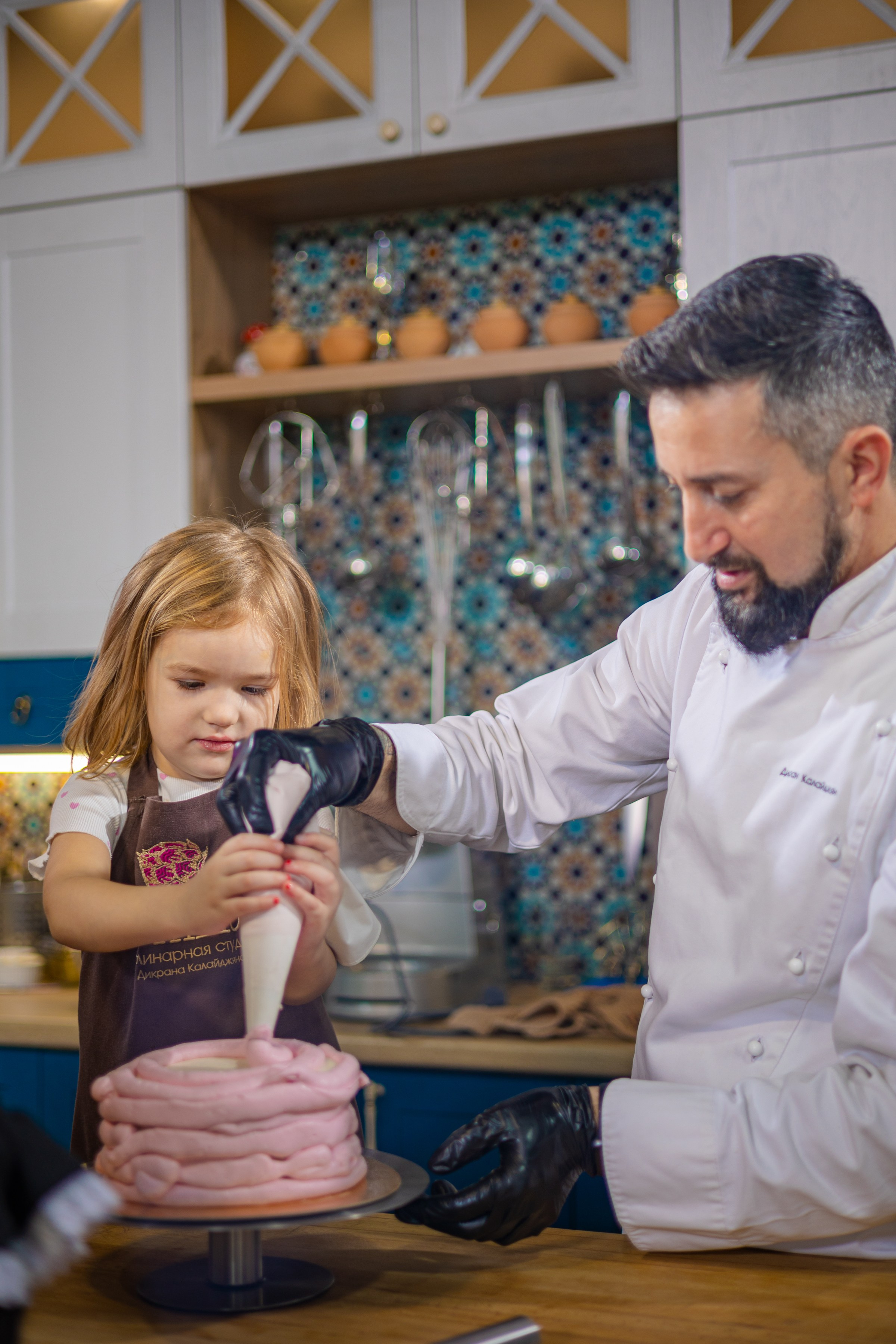 Кулинарная студия артишок шеф Дикран помогает ребёнку нанести крем на розовый торт