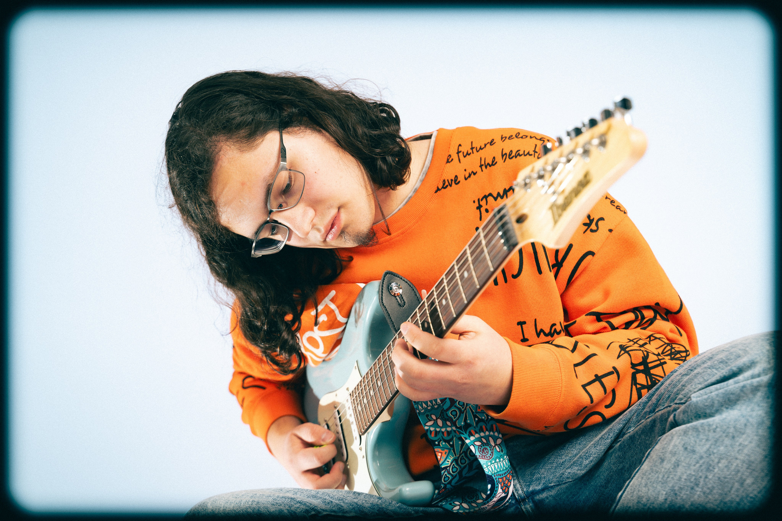 Молодой парень позирует в студии в яркой оранжевой одежде с гитарой