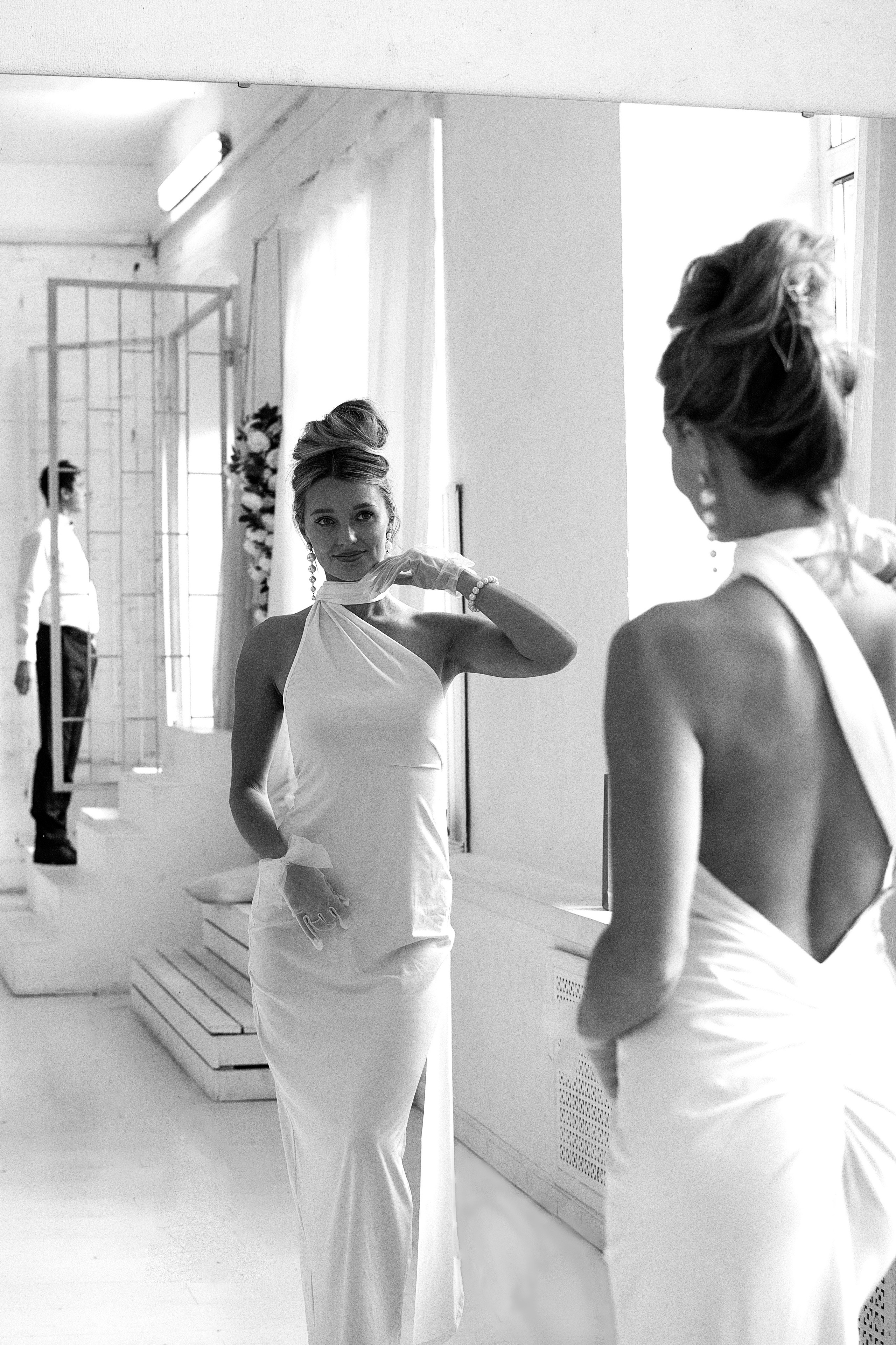 Невеста любуется собой у зеркала, жених смотрит на нее