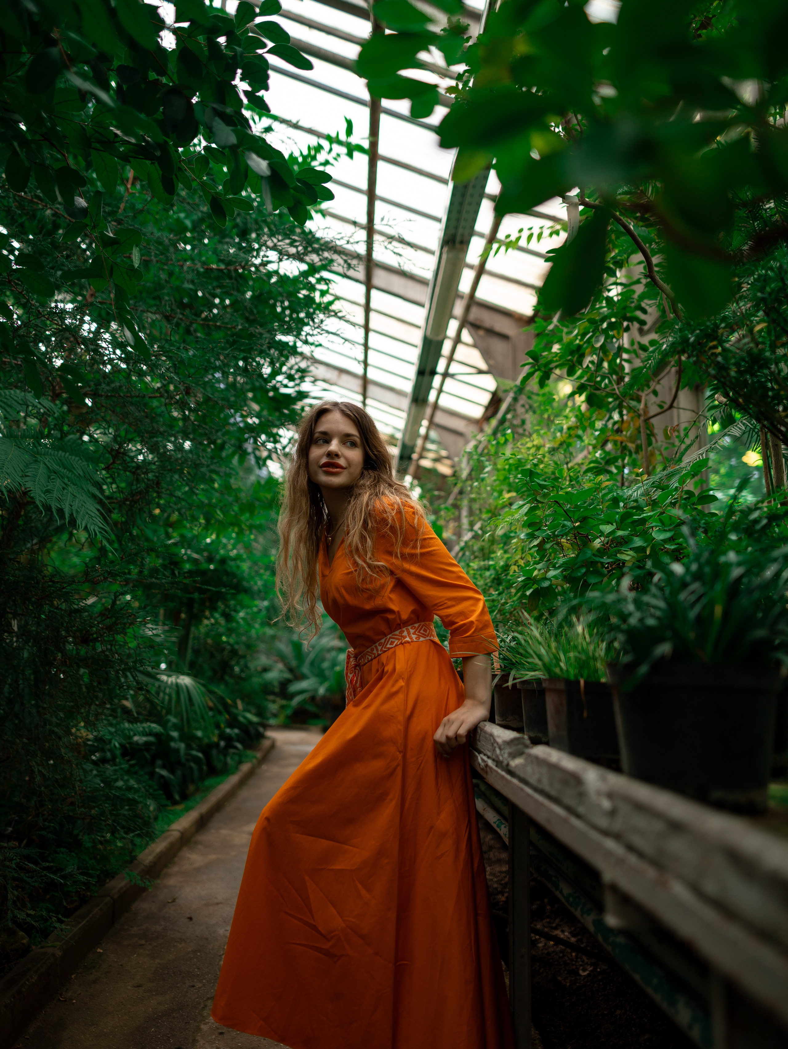 Девушка в оранжевом платье стоит на фоне зелени