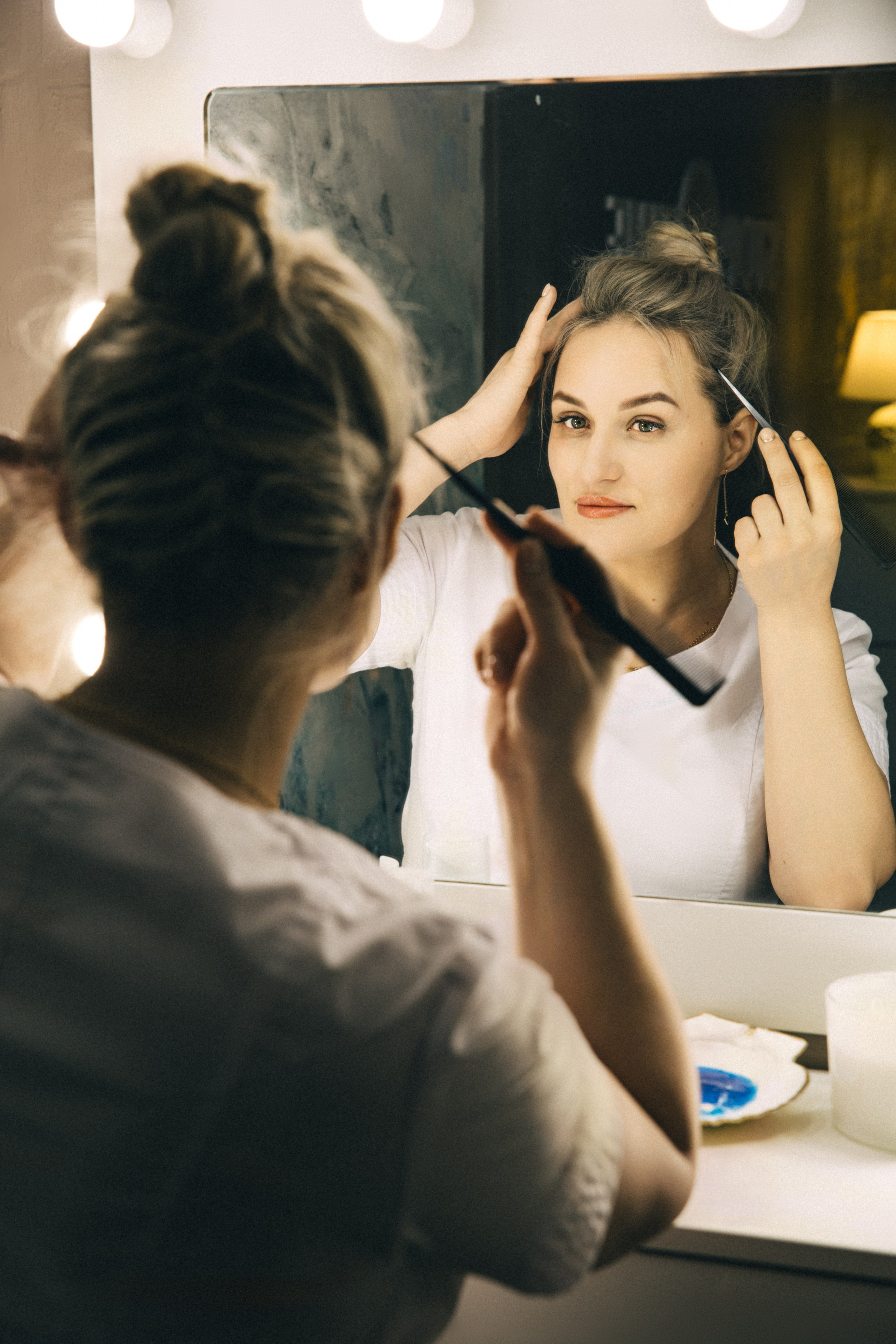 девушка расчесывает волосы и смотрит в зеркало