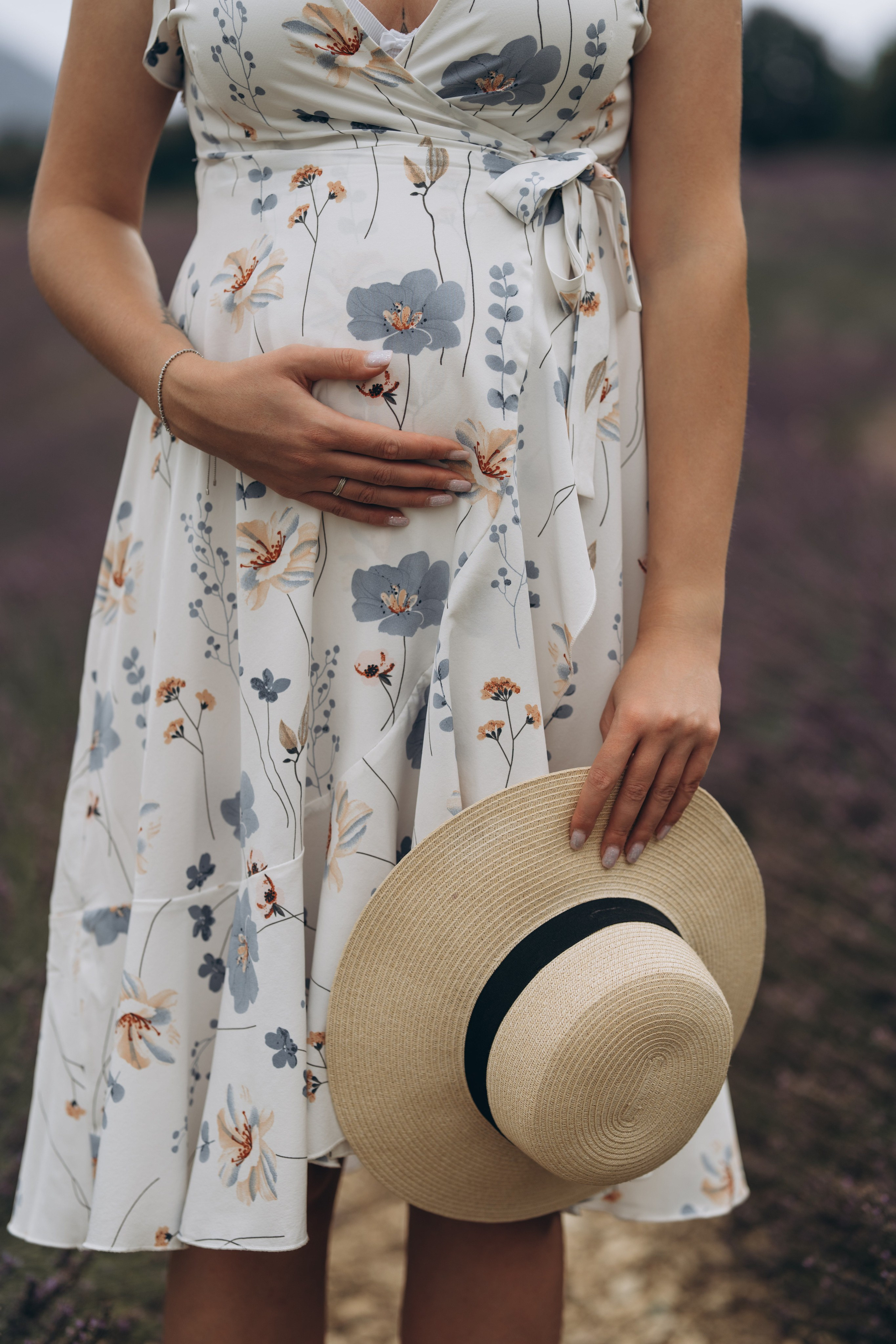 Femme enceinte debout dans un champ, robe fleurie et chapeau à la main, Provence