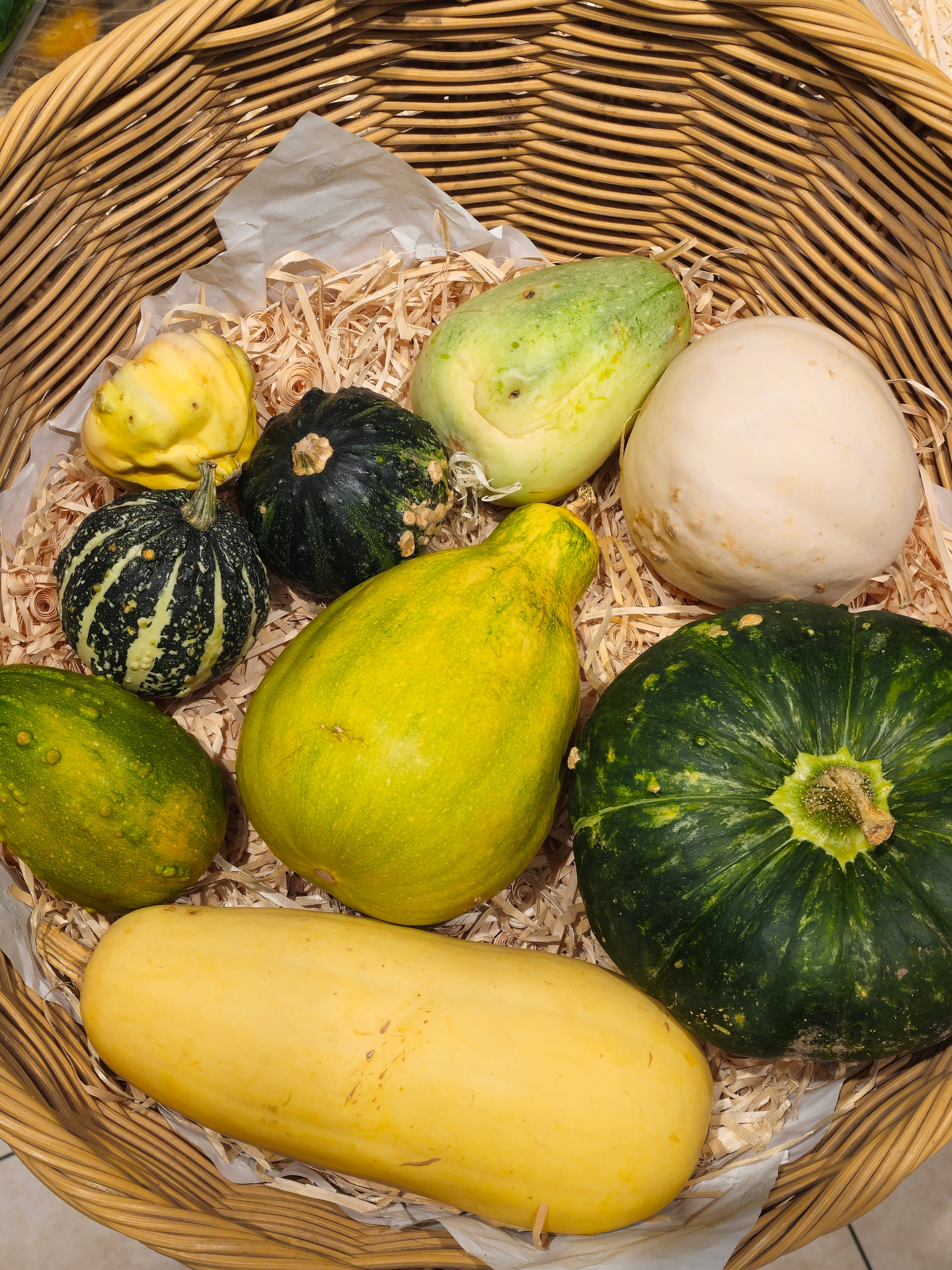Корзина с несколькими разноцветными тыквами и кабачками на фоне соломы.