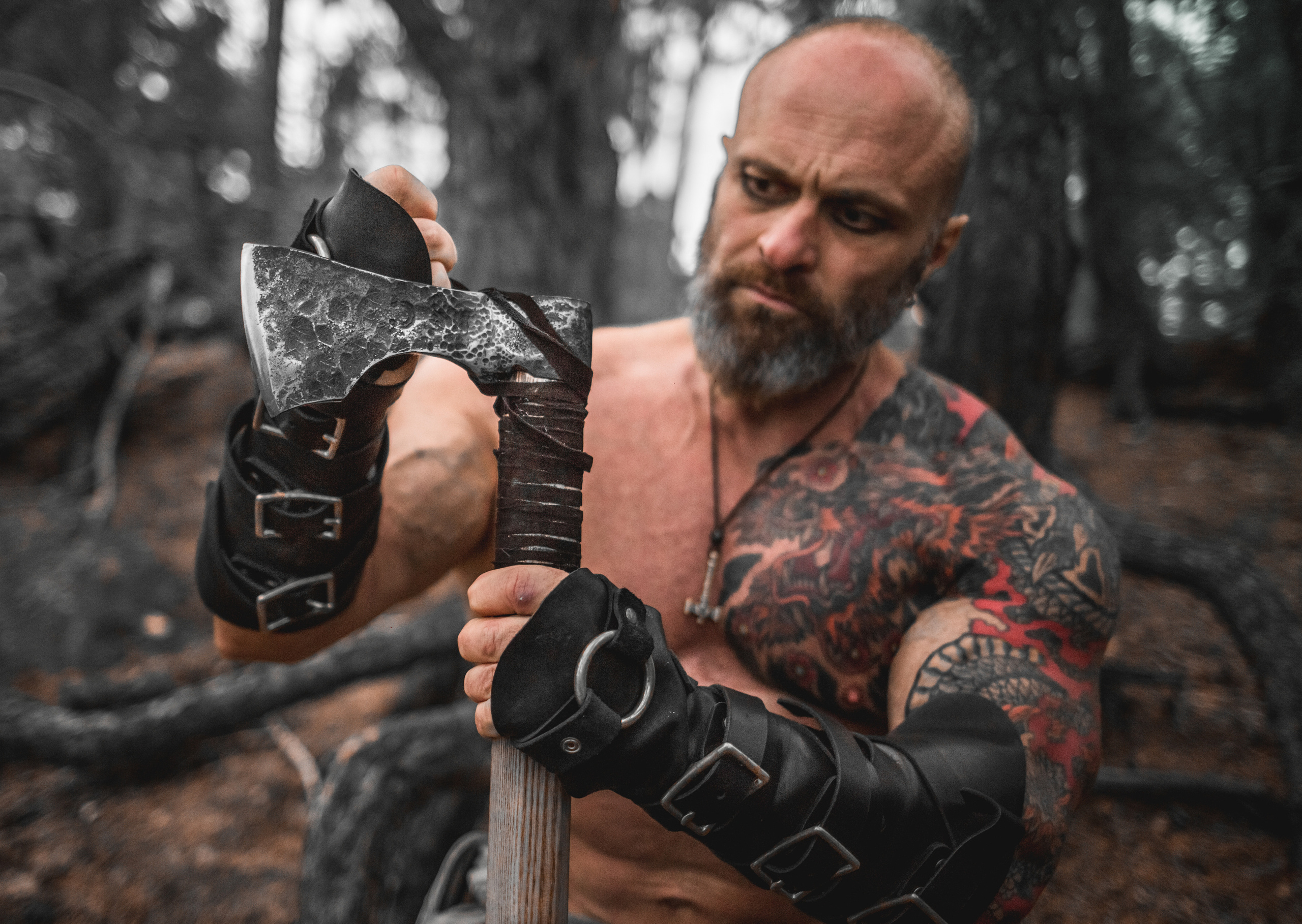 бодибилдер викинг точит топор. Ночная фотосессия среди корней старых деревьев с дымом и огнем.