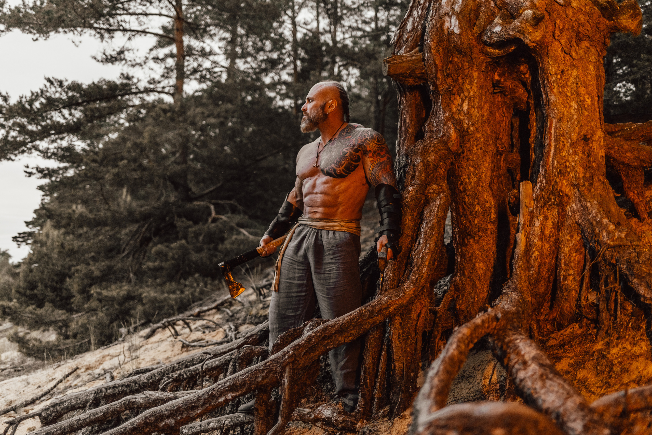 бодибилдер фотосессия в стиле викинги. Ночная фотосессия среди корней старых деревьев с дымом и огнем.