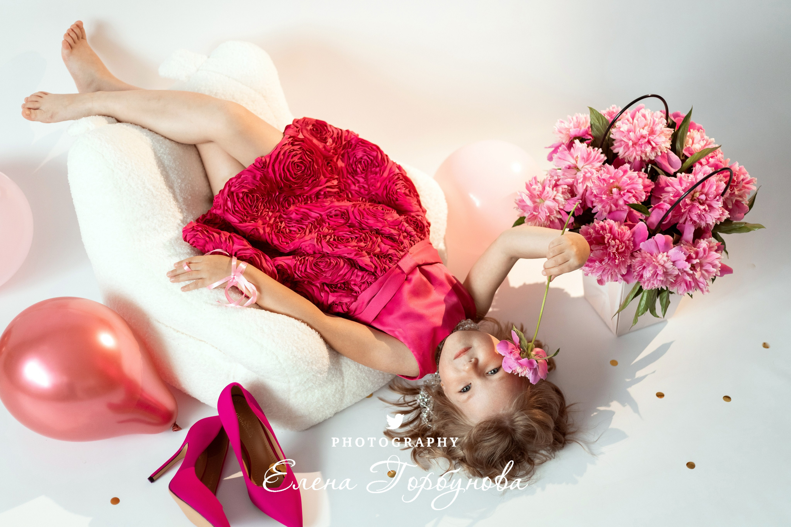 девочка модница в розовом с пионами на кресле вниз головой на фотосессии в студии