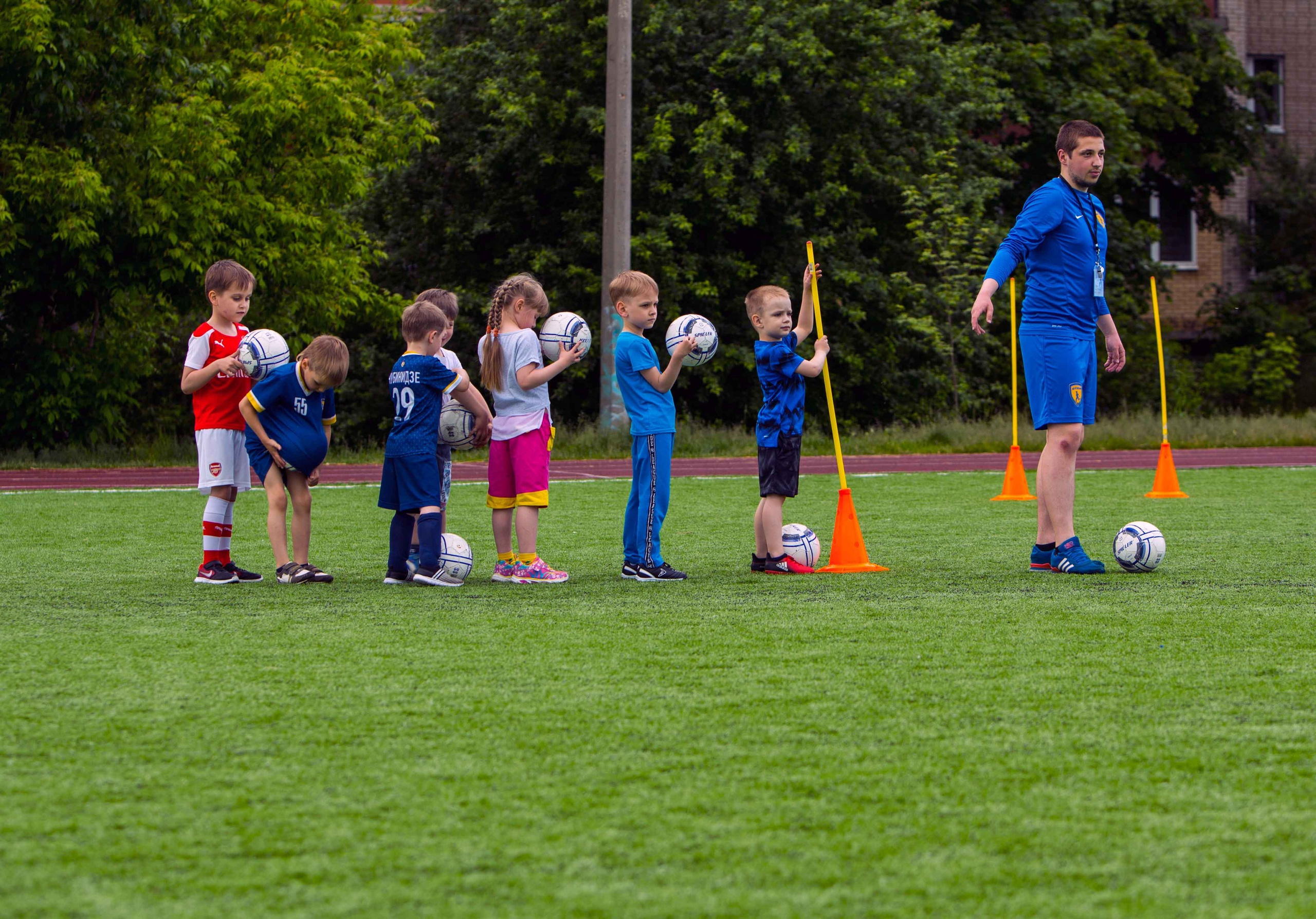 Дети на тренировке в футбольной школе «Юниор» выполняют задания под руководством тренера