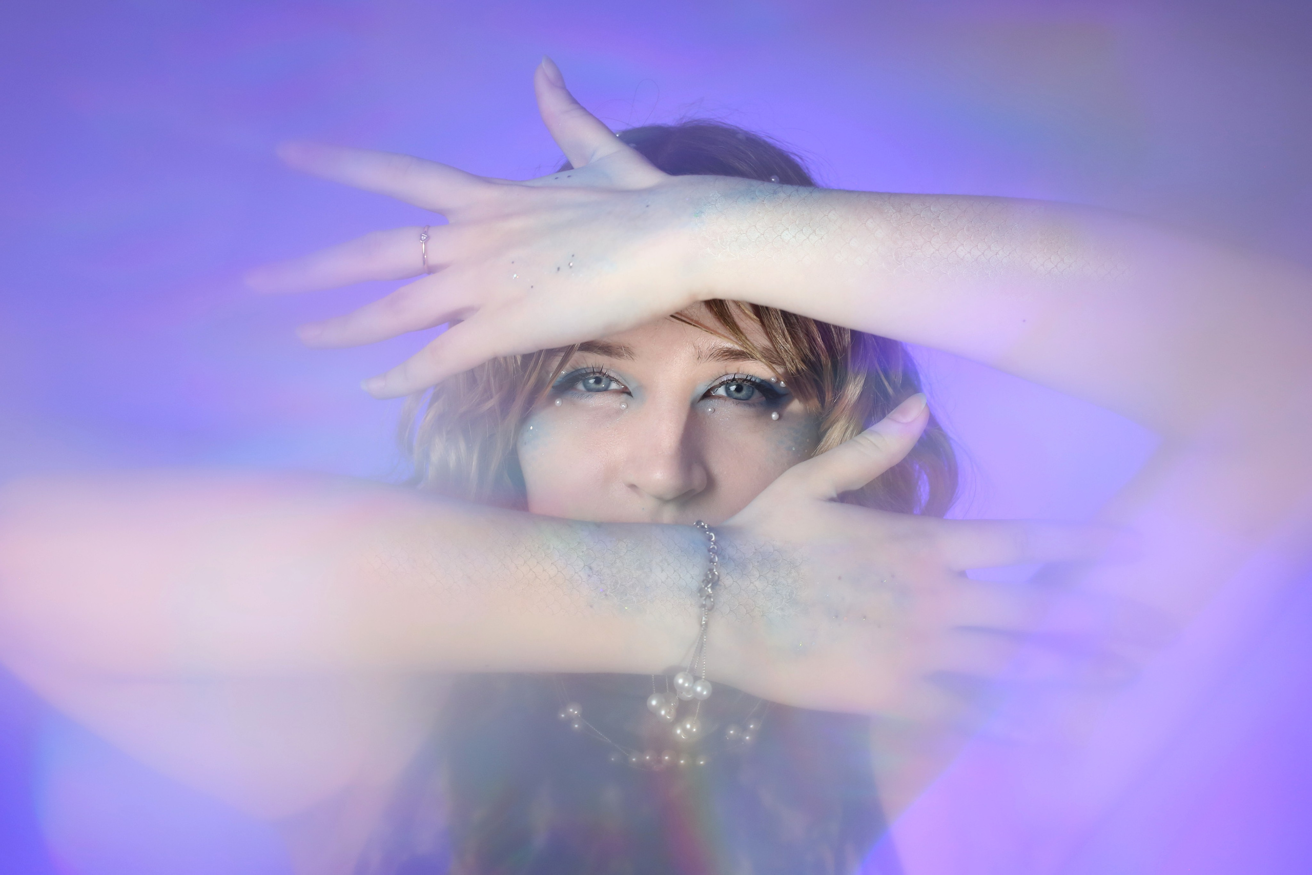 Творческая съемка «Ундина»: девушка закрывает лицо руками на фоне фиолетового света