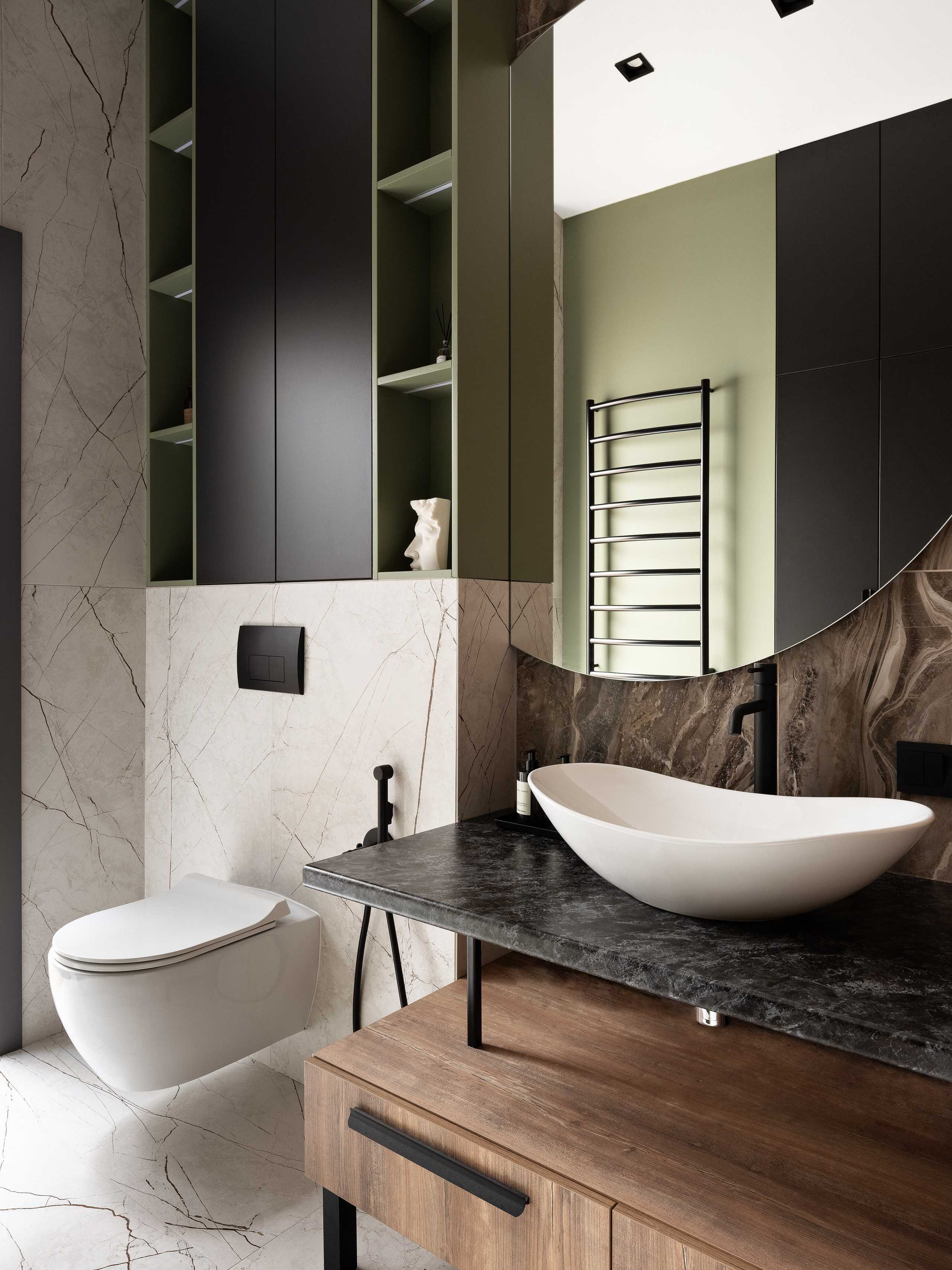 Интерьер светлой ванной комнаты с настенным унитазом, зелеными и черными шкафами, овальной раковиной и мраморной плиткой с прожилками; автор проекта дизайнер Екатерина Мищенко, фотограф Сергей Денисенко.