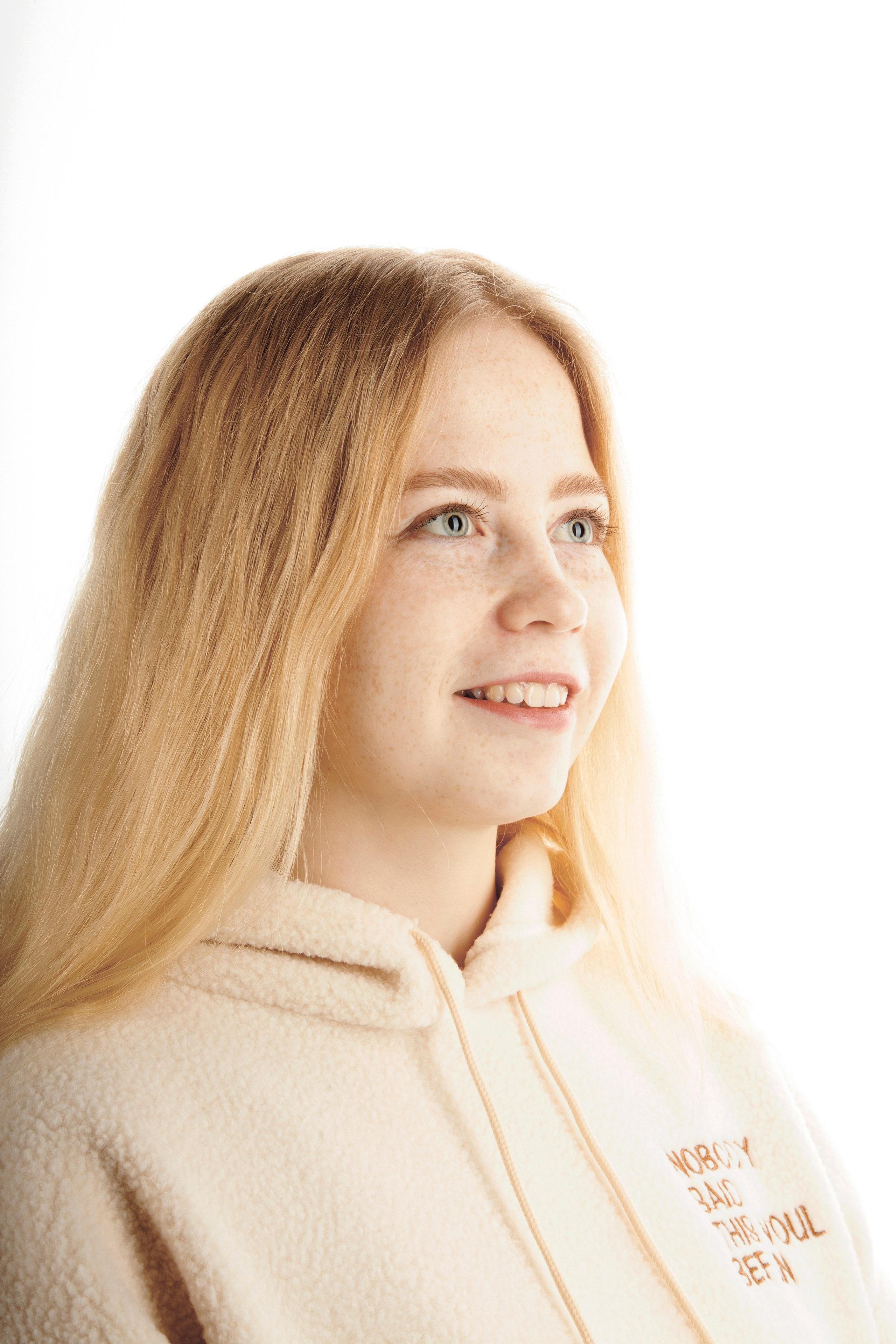 Портрет светловолосой и голубоглазой девушки с веснушками. В светлой одежде на белом фоне.