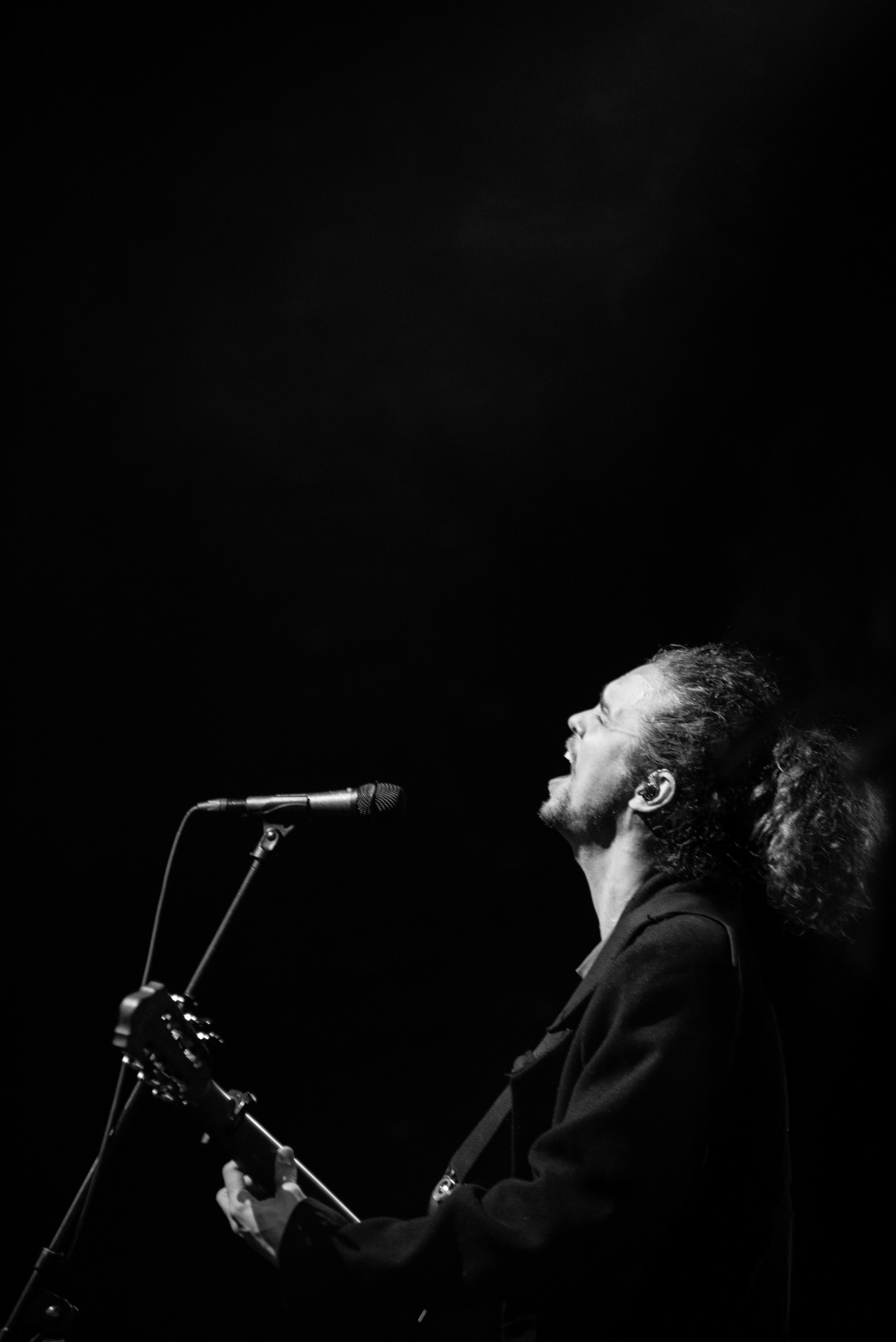 Чёрно-белый кадр вокалиста группы «Лампабикт» с гитарой у микрофона на сцене