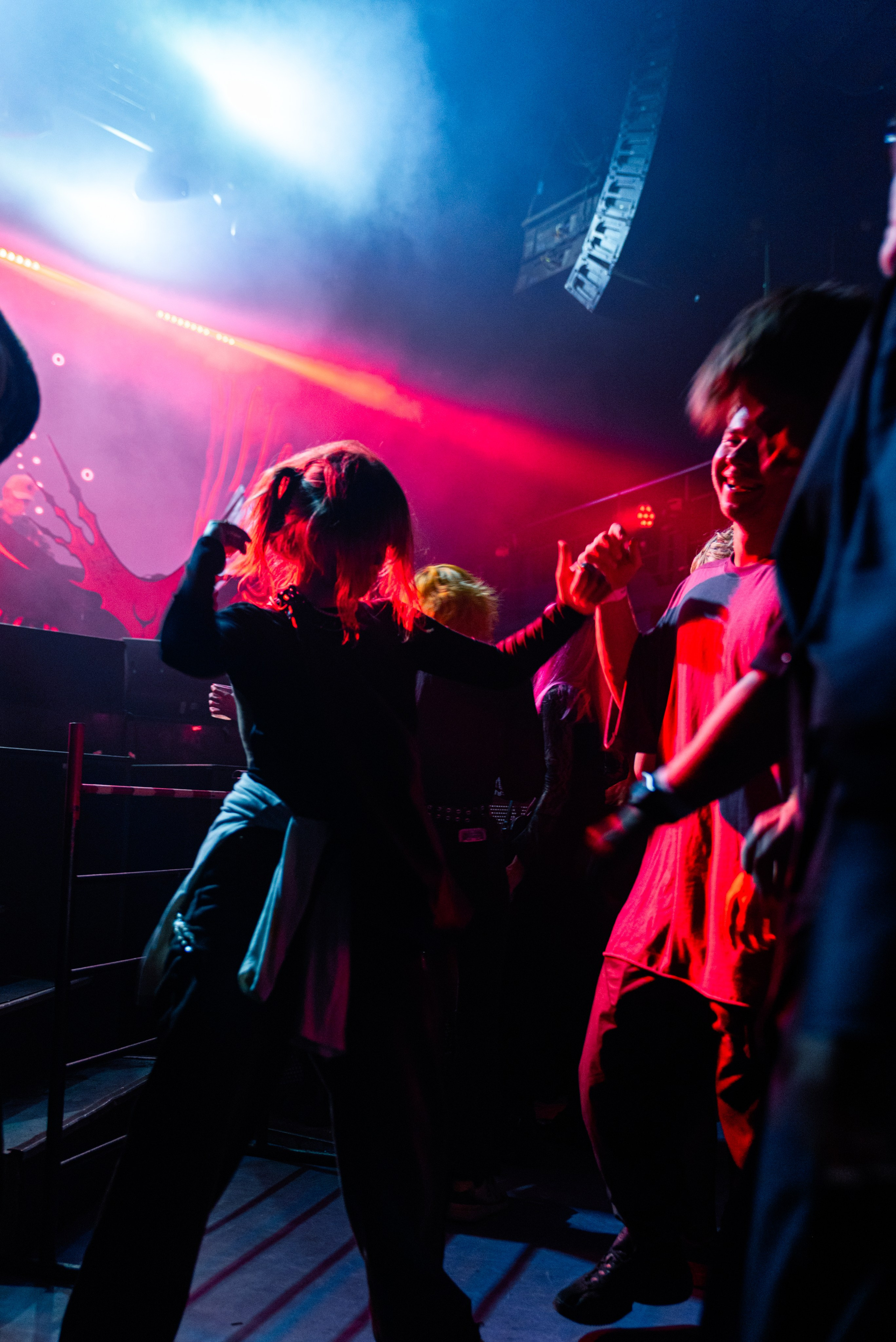 Концерт, люди танцуют в зале, красно-синий свет, движения чуть смазаны