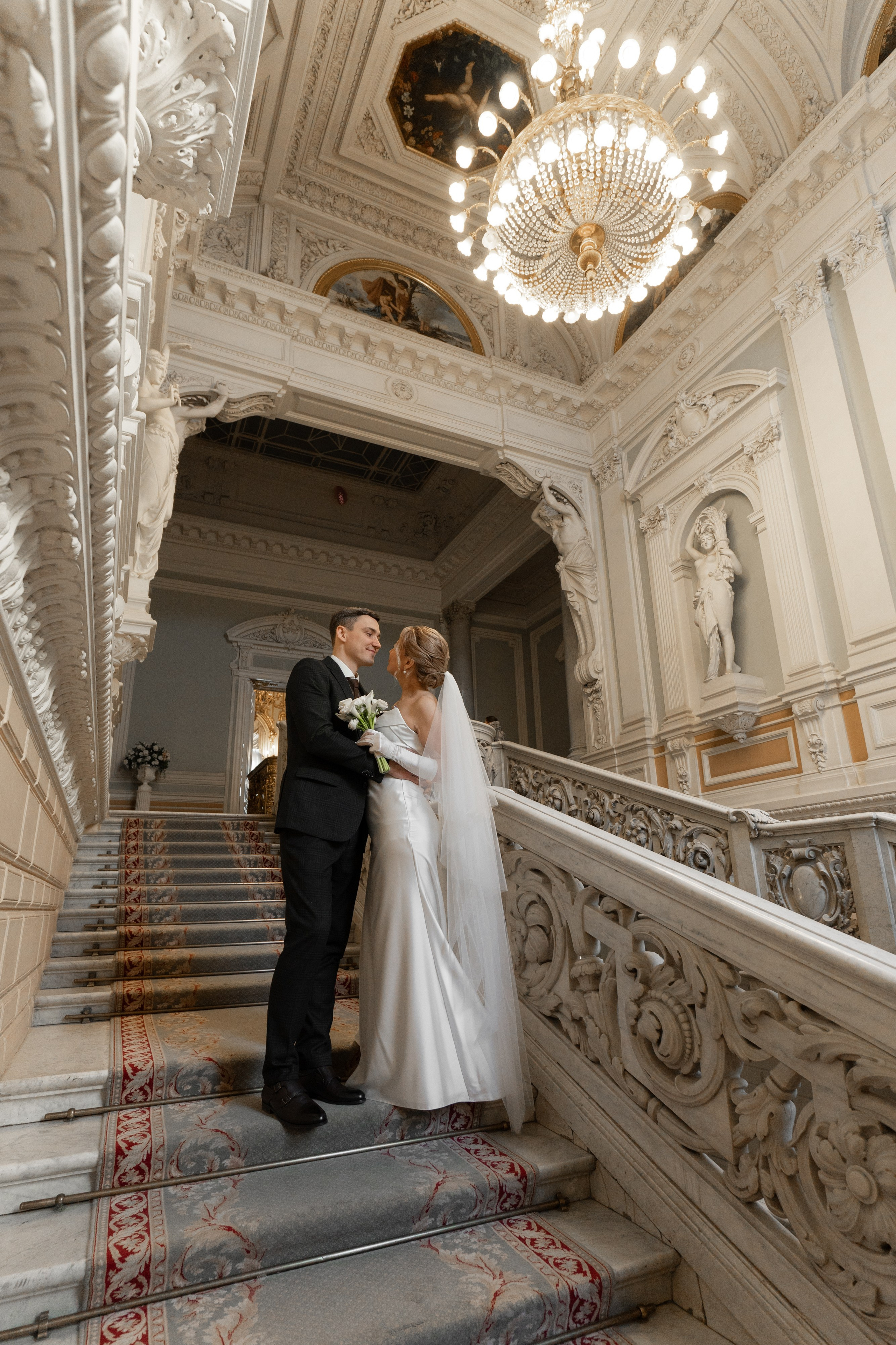 Свадебная фотосессия во Дворце Бракосочетания №1 Жених и невеста в белом платье стоят на красивой лестнице.