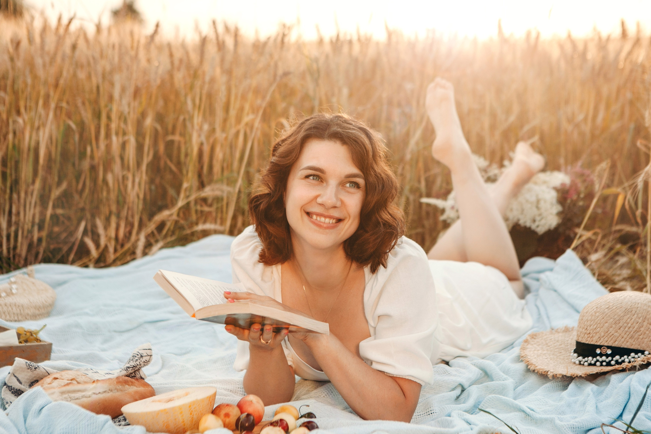 Девушка лежит на пшеничном поле и читает книгу 