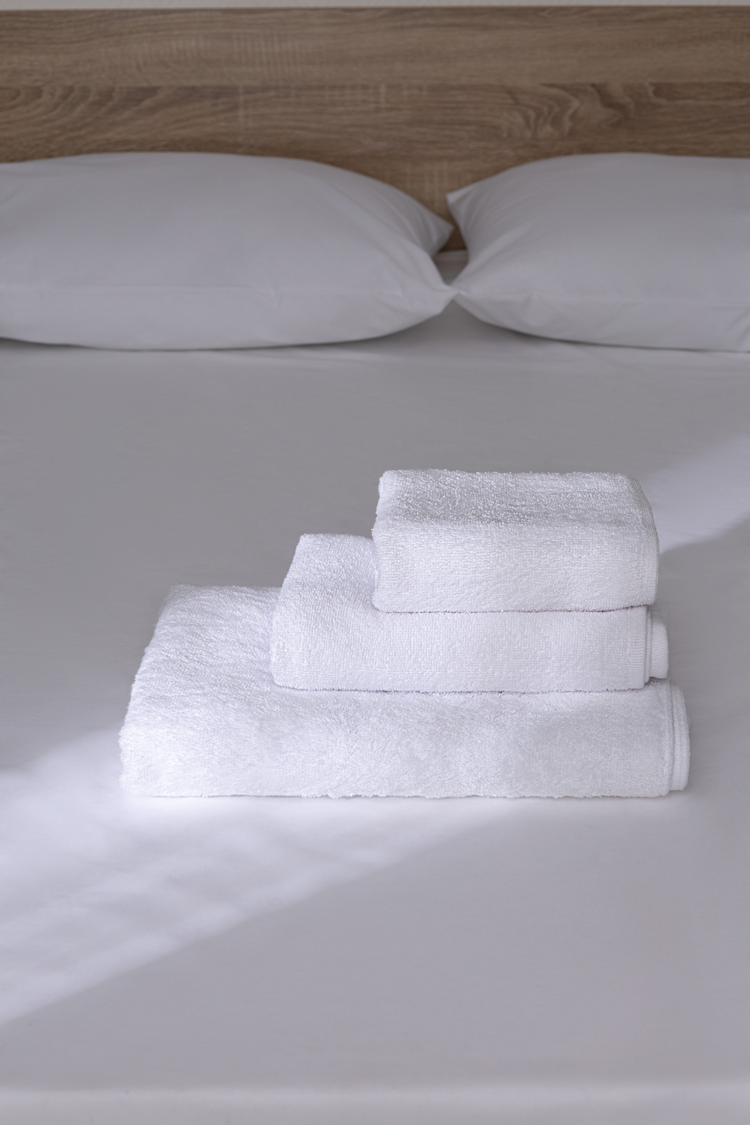 Белые полотенца сложенные стопкой на кровати | Фото для сайта производителя текстиля