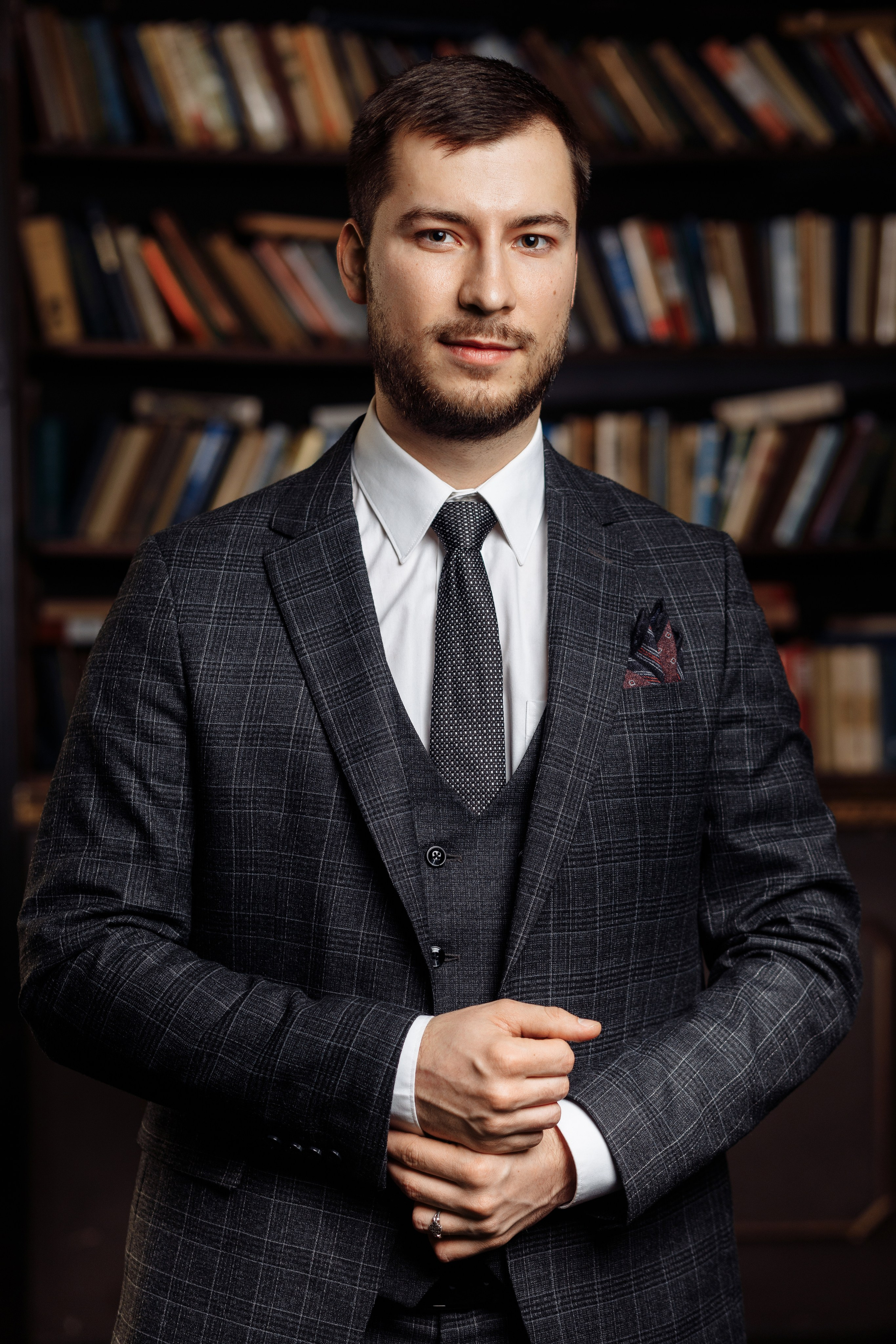 Портрет мужчины, который позирует на фоне книжных полок в библиотеке.