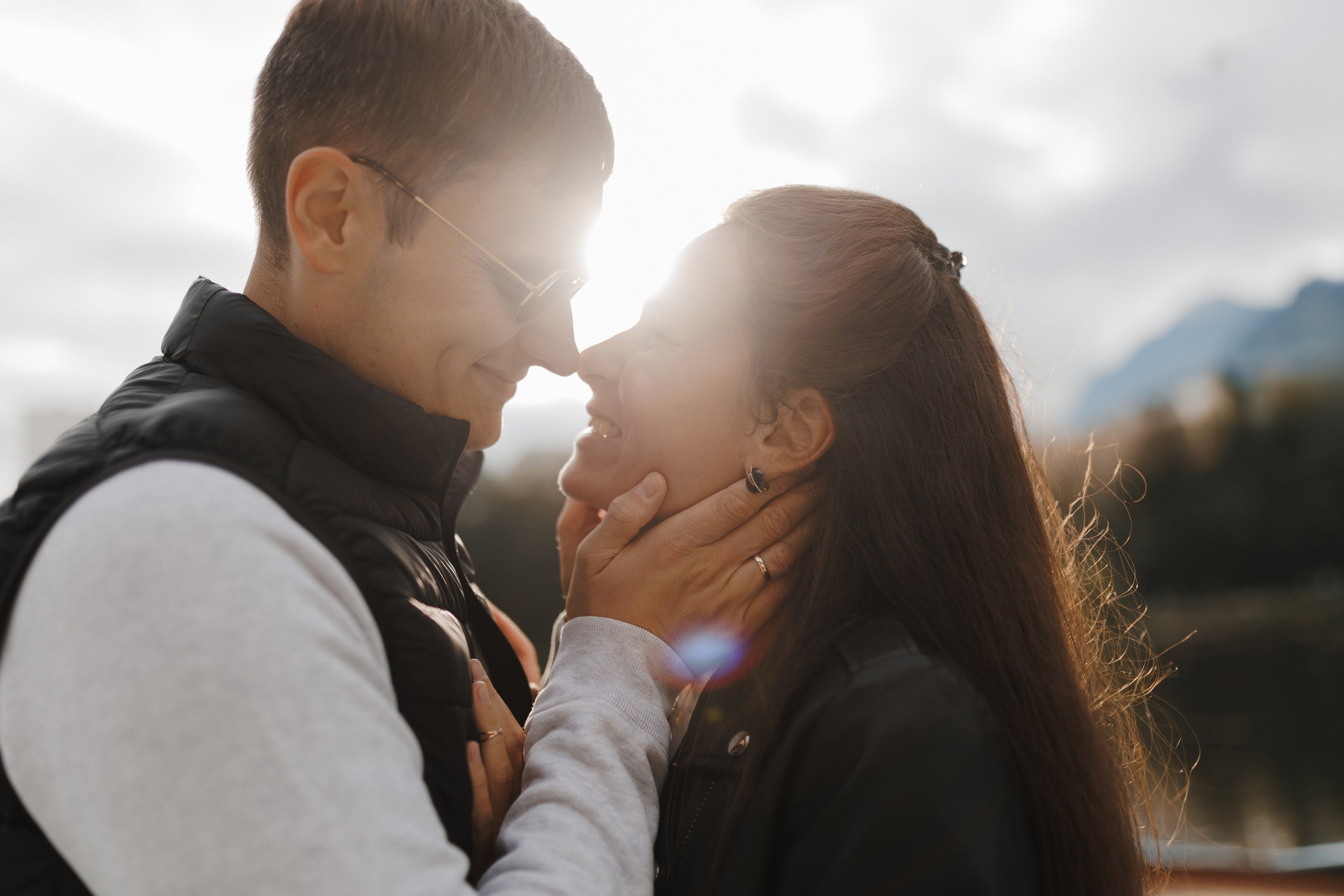 Крупный план: пара обнимается и смотрит друг другу в глаза на фоне закатного неба. Интимный и тёплый портрет.