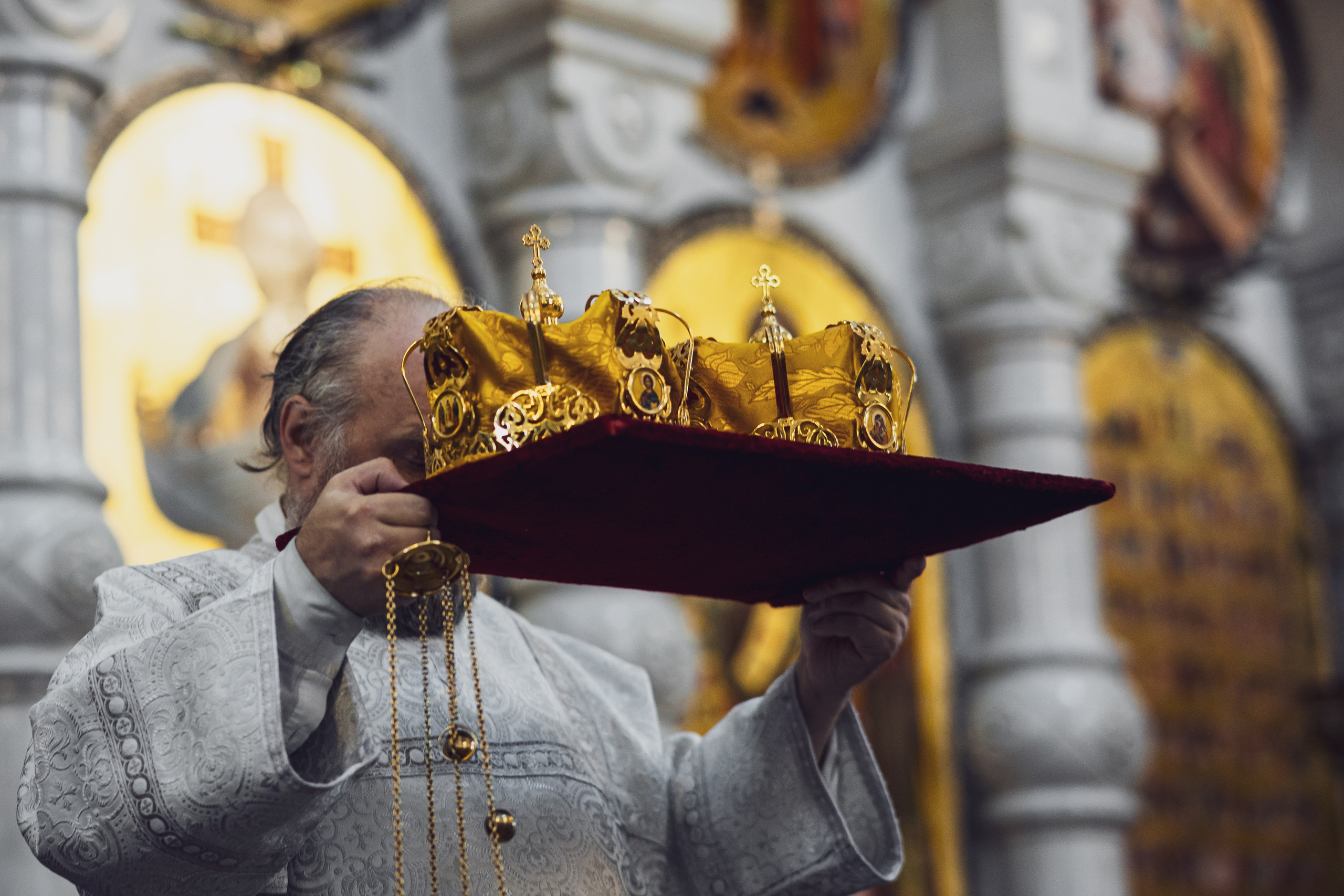 Священник держит венцы на подносе перед венчанием, золотой свет иконостаса — Екатеринбург, Илья Антропов