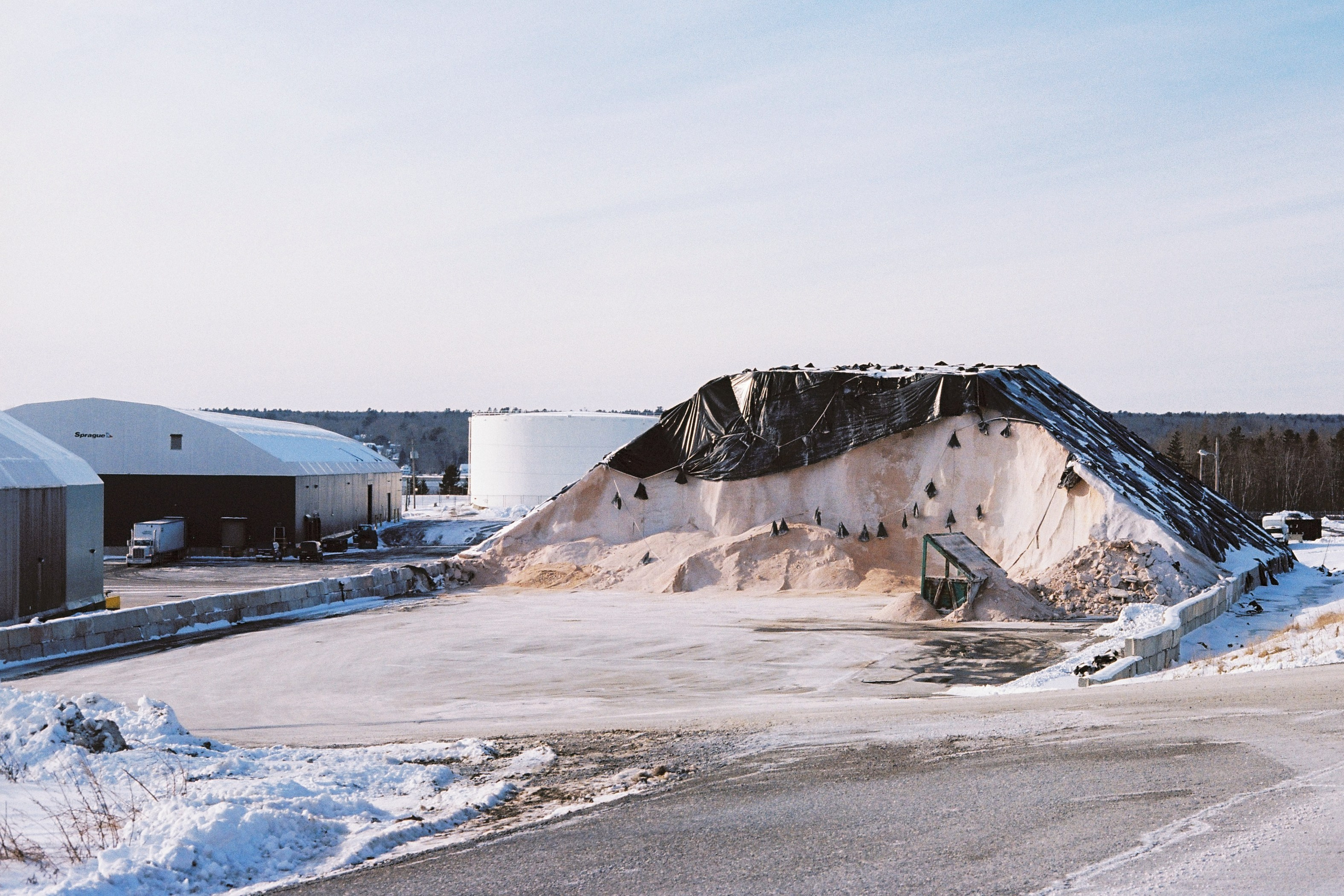Вид из морского терминала на огромную гору песка, которая выше ангаров и грузовиков. США