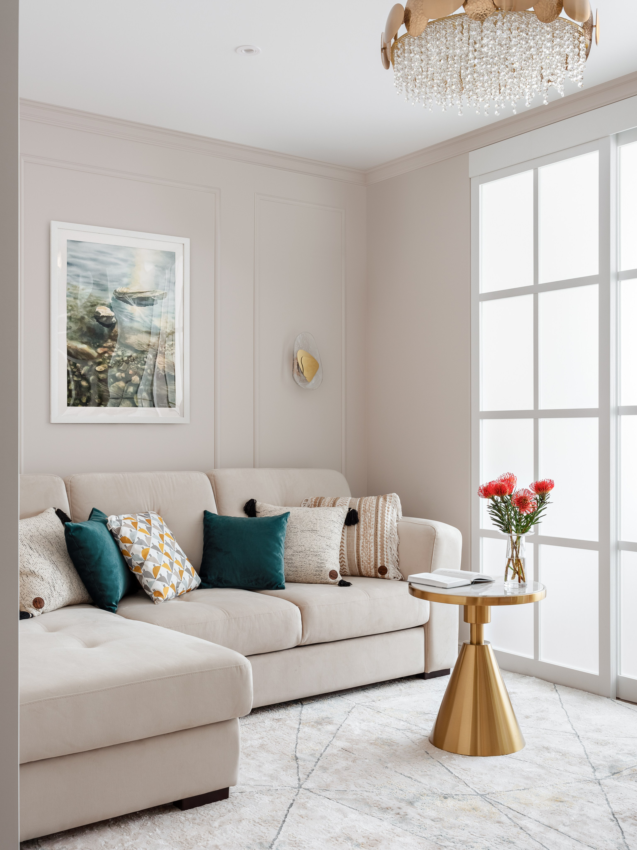 Светлый интерьер гостиной с диваном угловой формы, подушками в зелёной и бежевой гамме, золотым журнальным столиком и хрустальной люстрой. Стены украшены картиной и декоративным бра. Автор дизайна Наталья Бунеева, стилист Наталья Якушева, фото Сергей Денисенко.