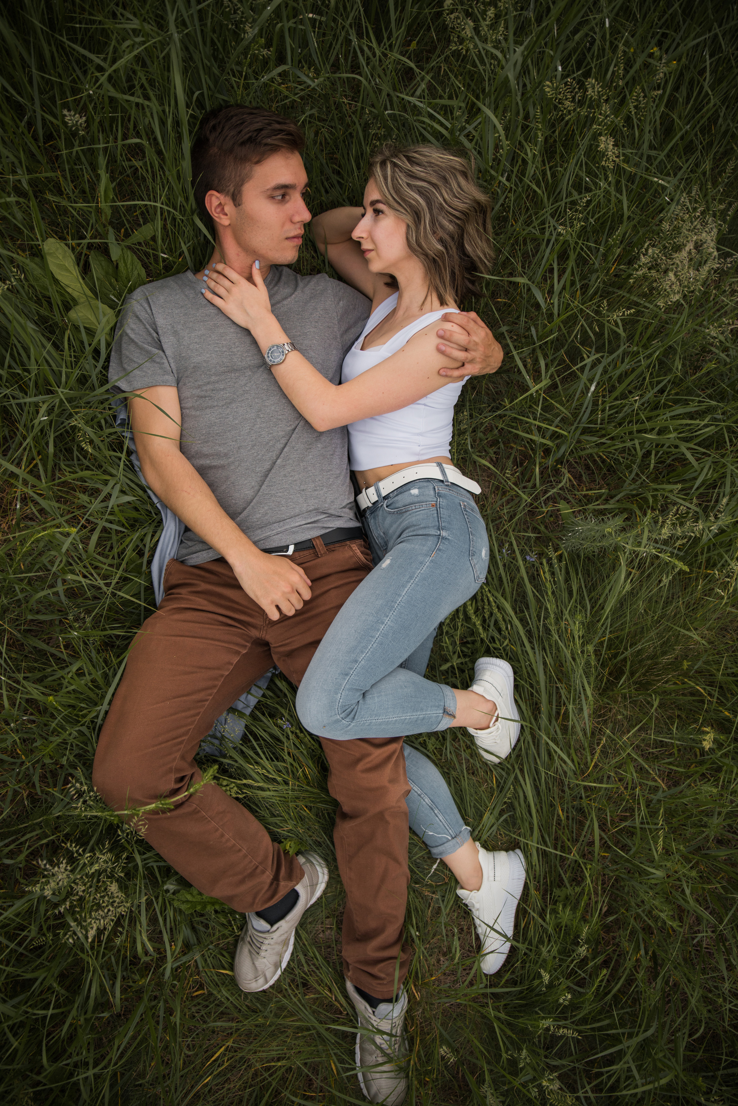 парень и девушка лежат в траве в объятиях друг-друга ракурс сверху