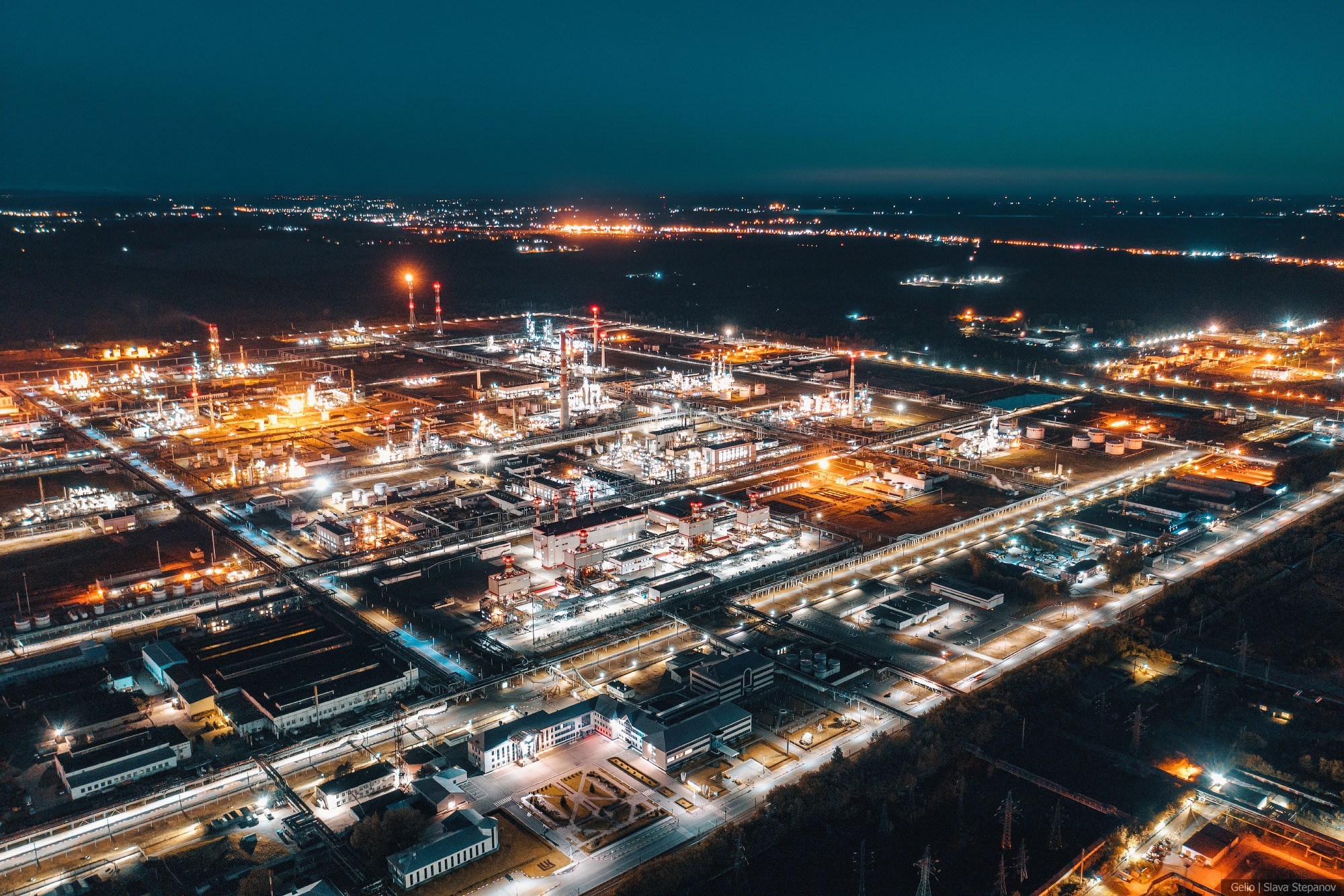Индустриальный масштаб ночного нефтехимического комплекса, вид с высоты на светящиеся ректификационные колонны, эстакады труб и производственные площадки, фото Slava Stepanov.