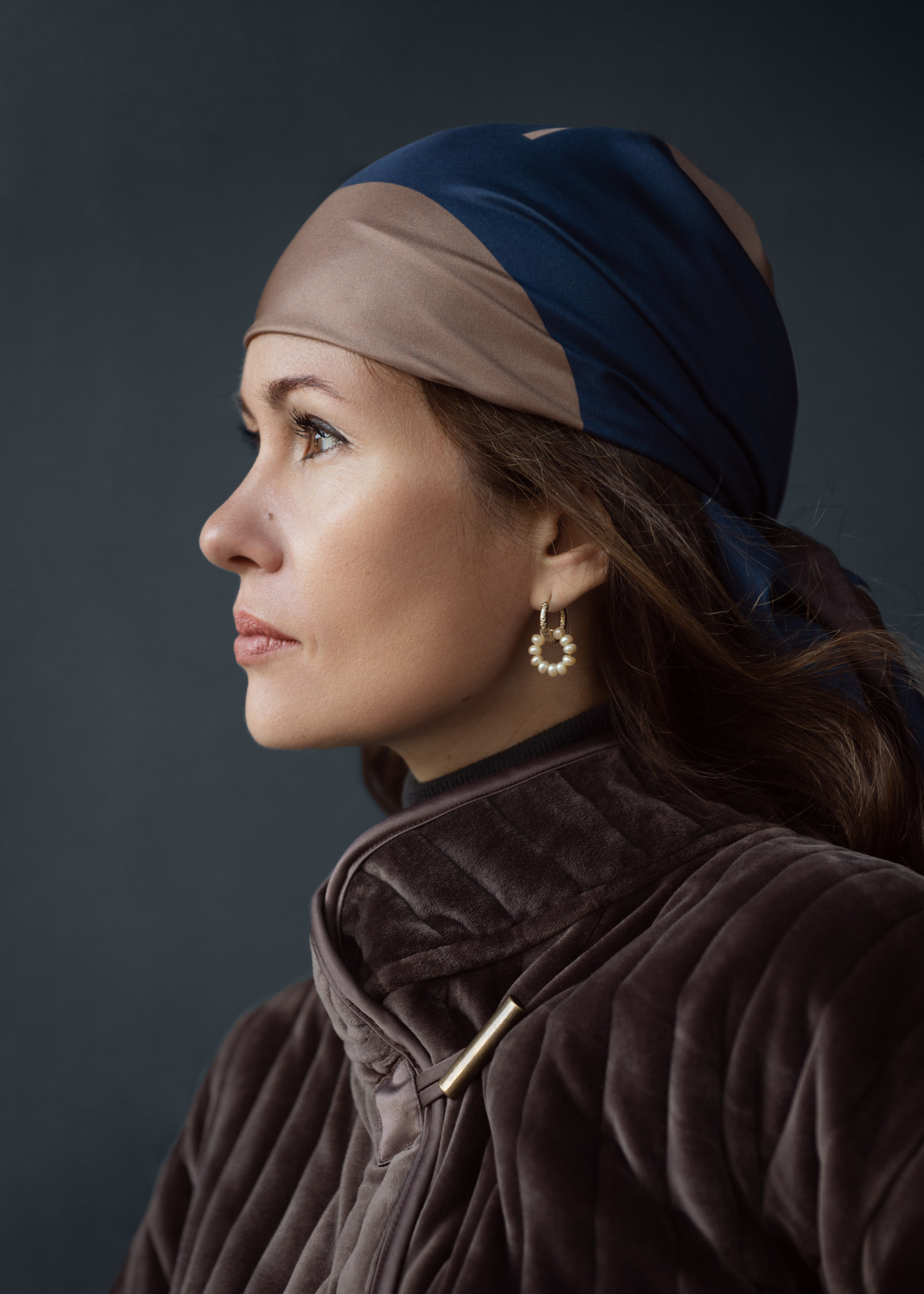 Портрет темноволосой девушки в профиль на темном фоне. Съемка для магазина женской одежды и аксессуаров. Мягкий естественный свет падает сверху и создает красивый свето-теневой рисунок на модели. Съемка на улице. Уличный портрет.