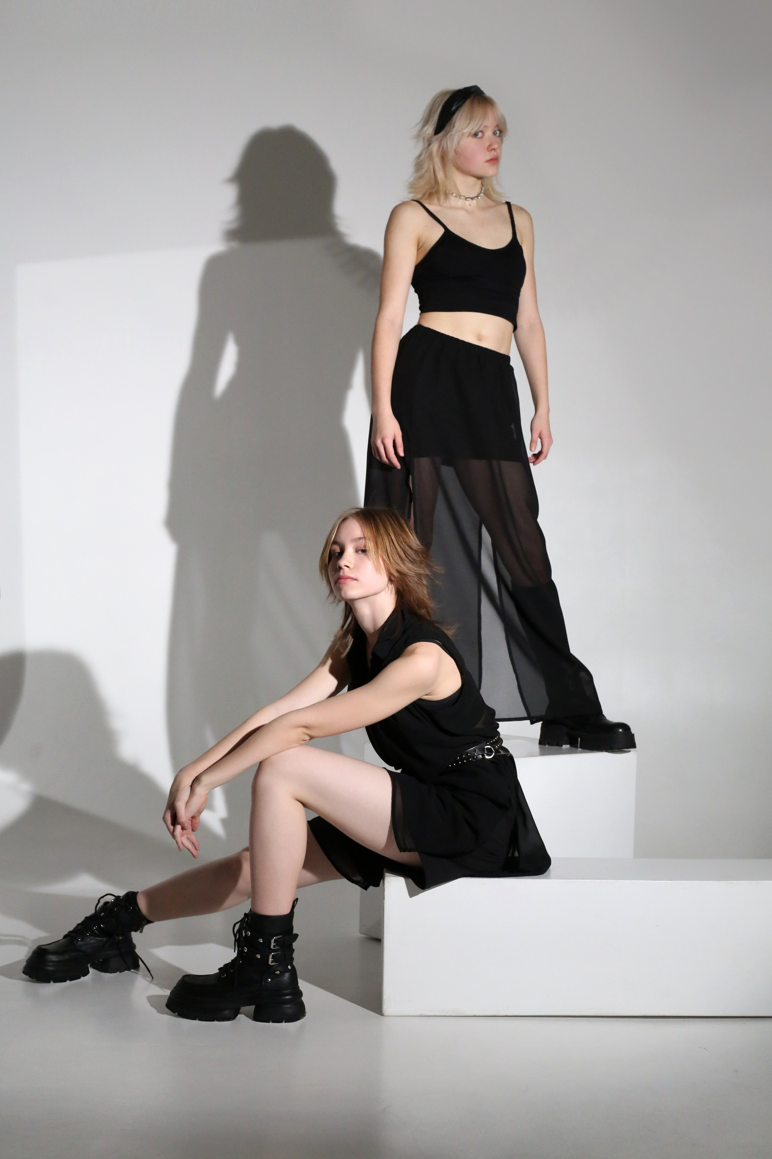 Минималистичная фотосессия: две девушки в черных костюмах позируют на белых кубах