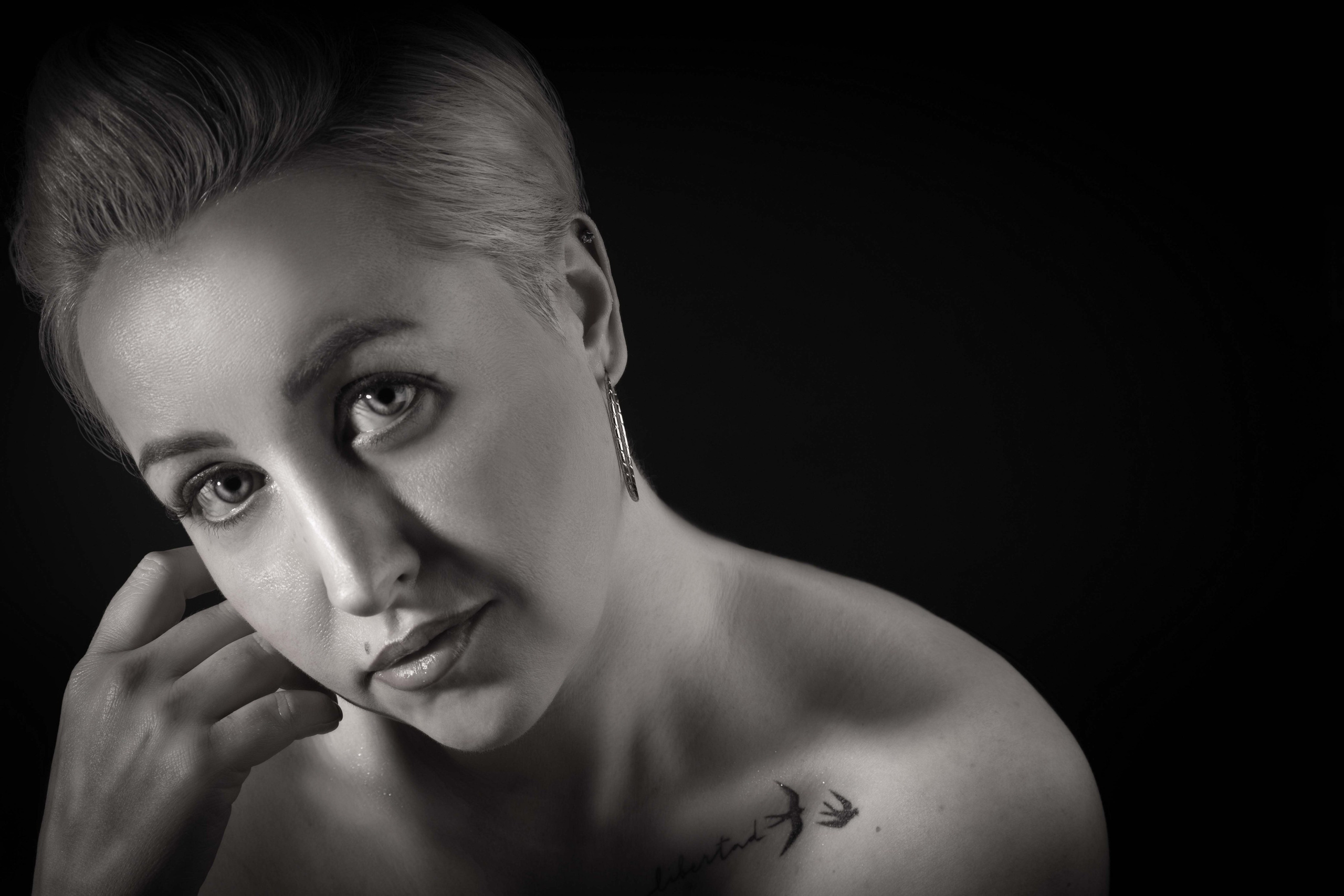 ЧБ портрет девушки. Выразительный взгляд, низкий ключ, детализация татуировки на ключице и текстуры кожи. Профессиональная студийная съемка