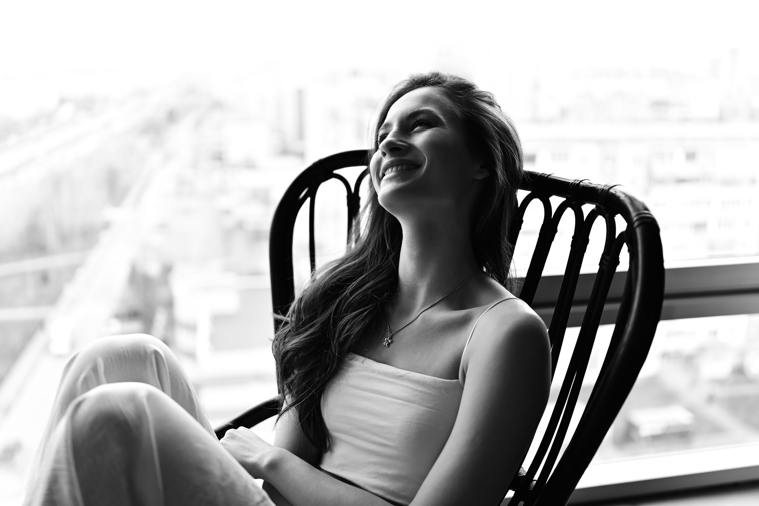 Девушка сидит в кресле в контровом свете от большого окна в черно-белом исполнении