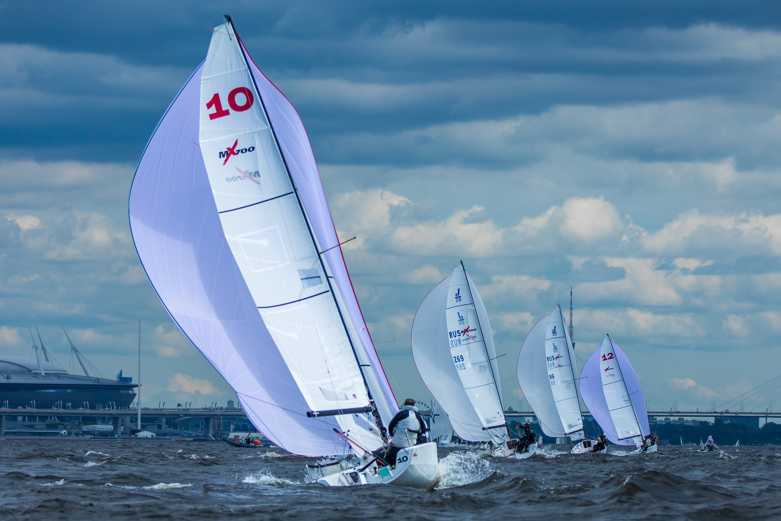 Яхты идут от верхнего знака на регате в Санкт-Петербурге. Белые паруса на фоне облаков.