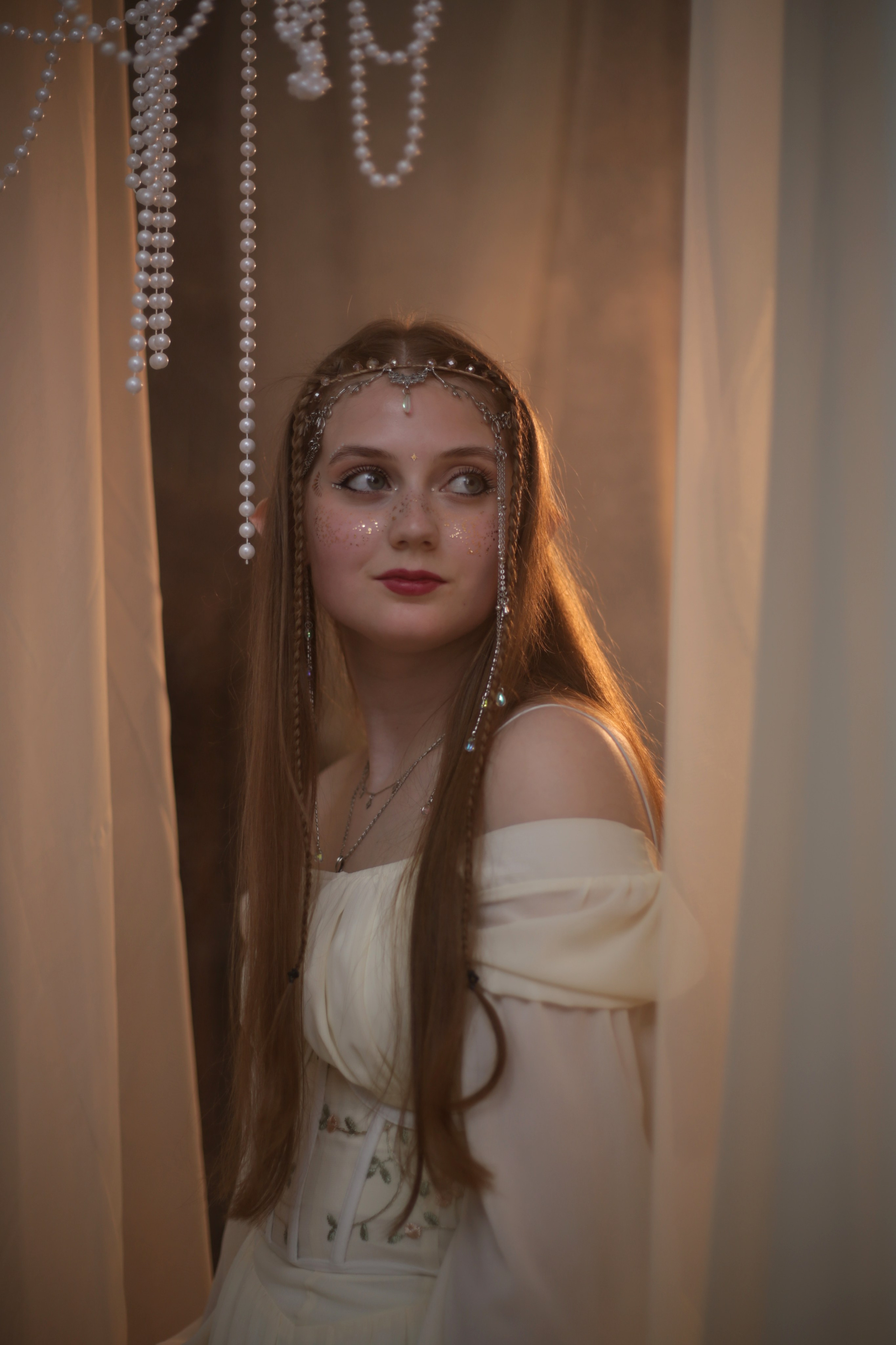 Эльфийская фотосессия: девушка в белом платье с поднятыми руками, лицо украшено блестками, атмосферное освещение