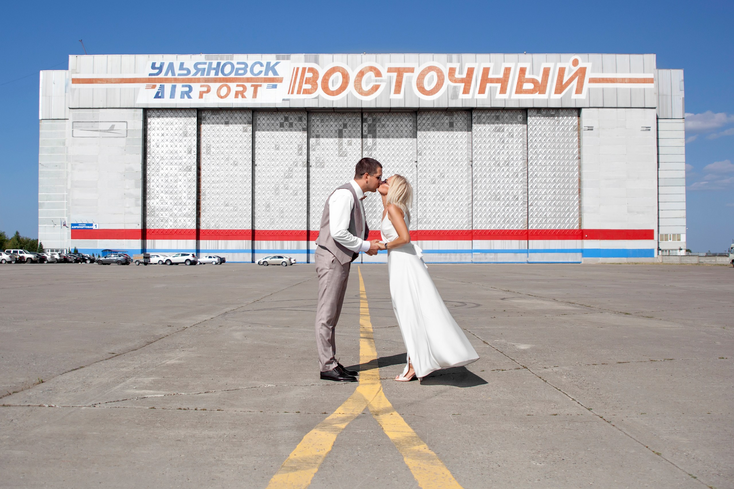 Жених и невеста целуются на фоне здания аэропорта Восточный