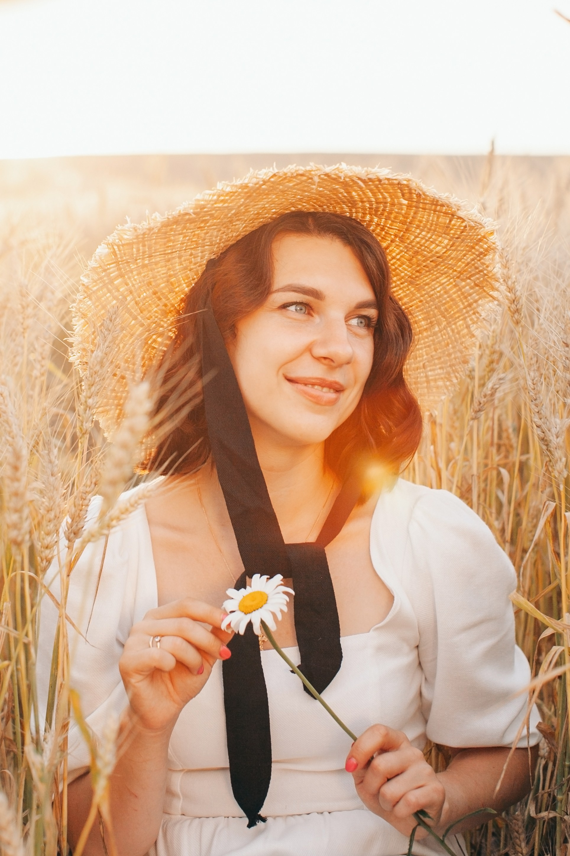 Девушка с ромашкой и в шляпке на фоне красивого закатного света