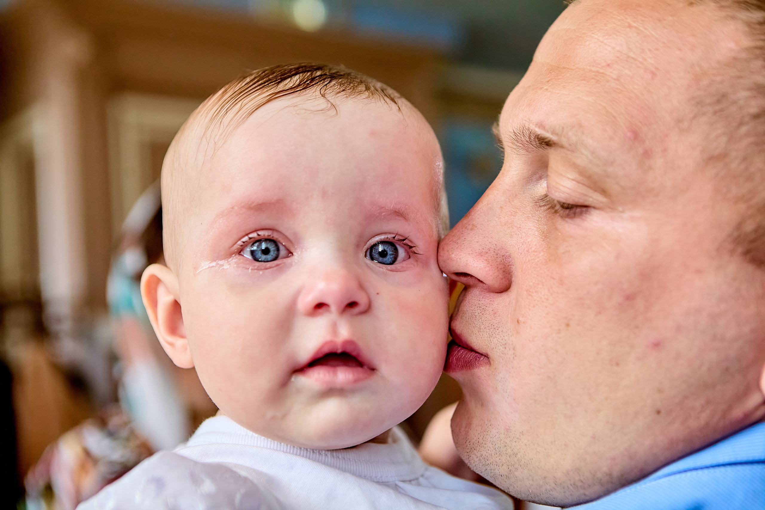 Молодой парень папа целует свою любимую дочку на таинстве крещения