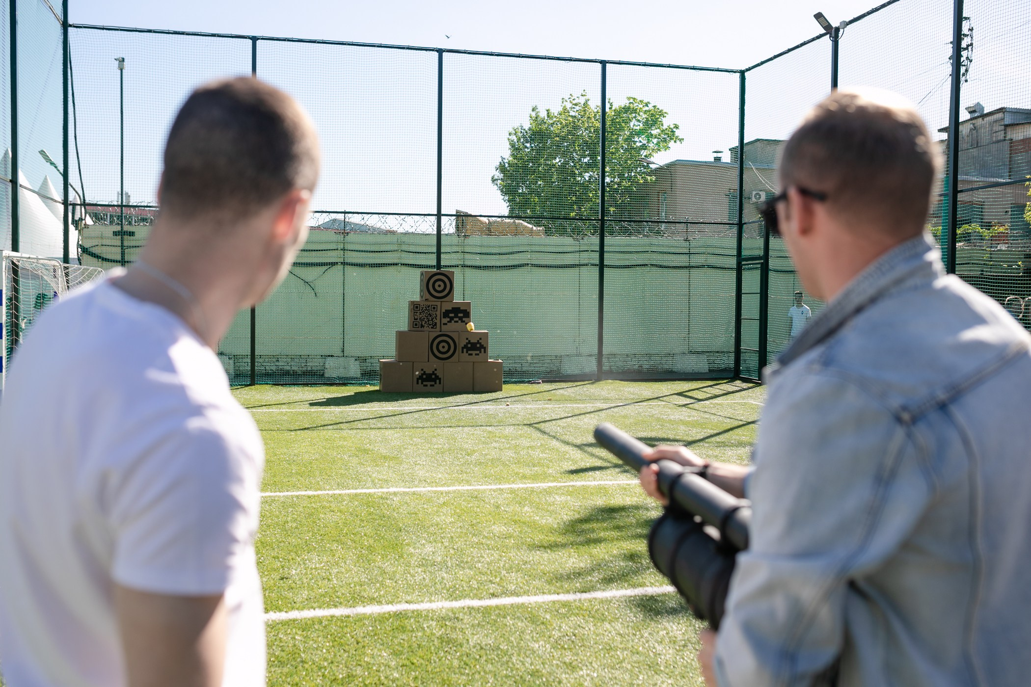 Мужчина стреляет из картофельной пушки в коробки сложенные в пирамиду
