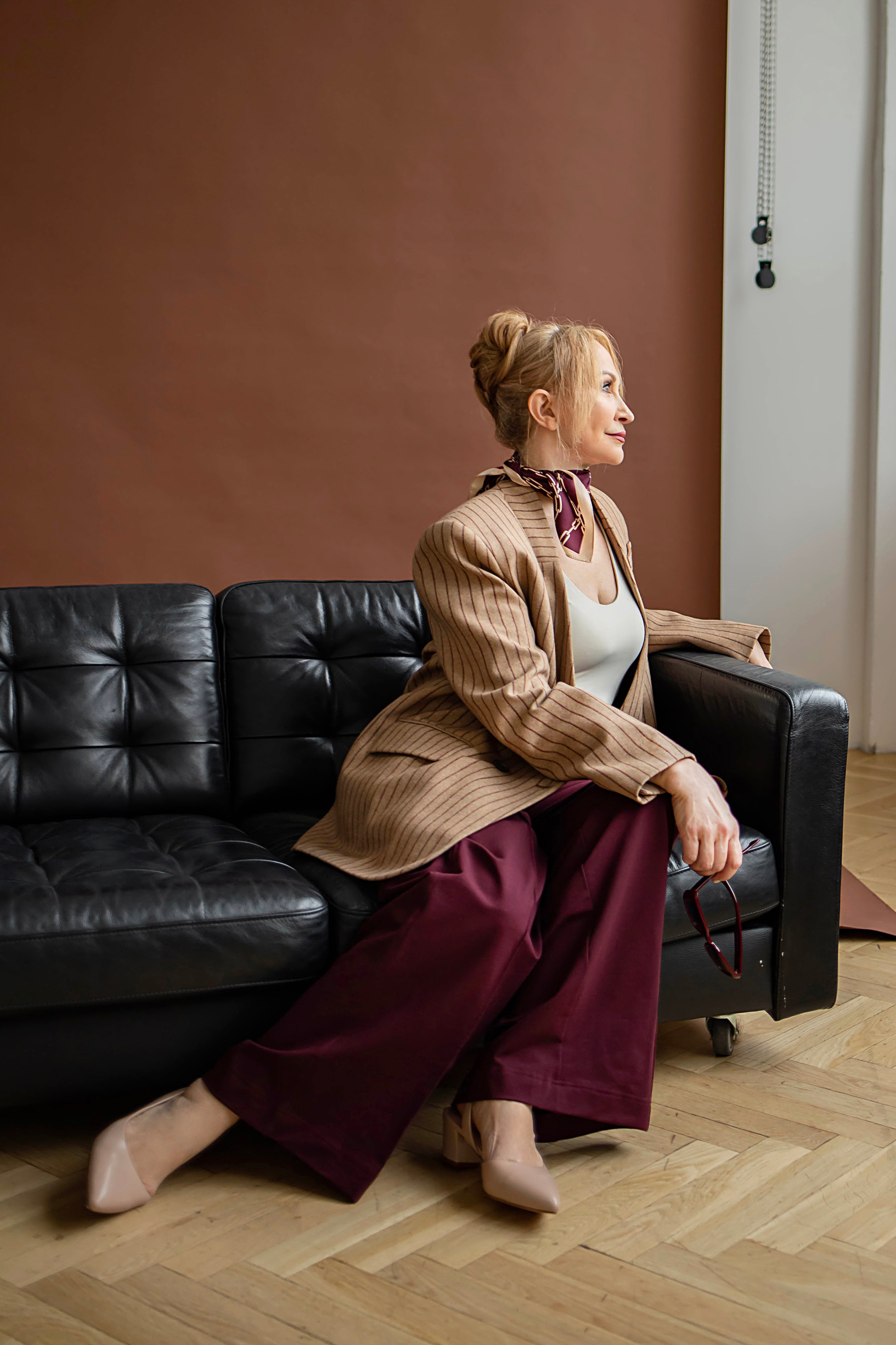 Девушка в брючном костюме позирует на черном кожаном диване, драматичный студийный портрет